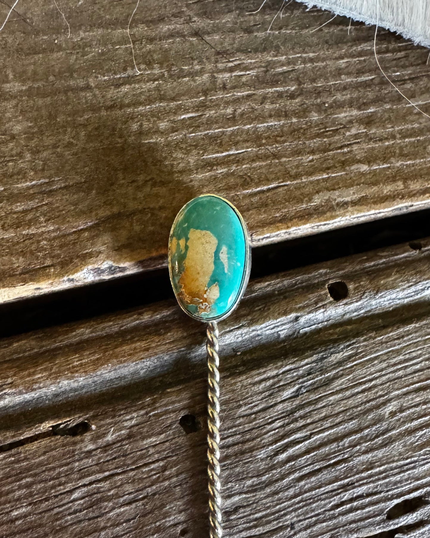 Pin with a green and gold design on a wooden surface