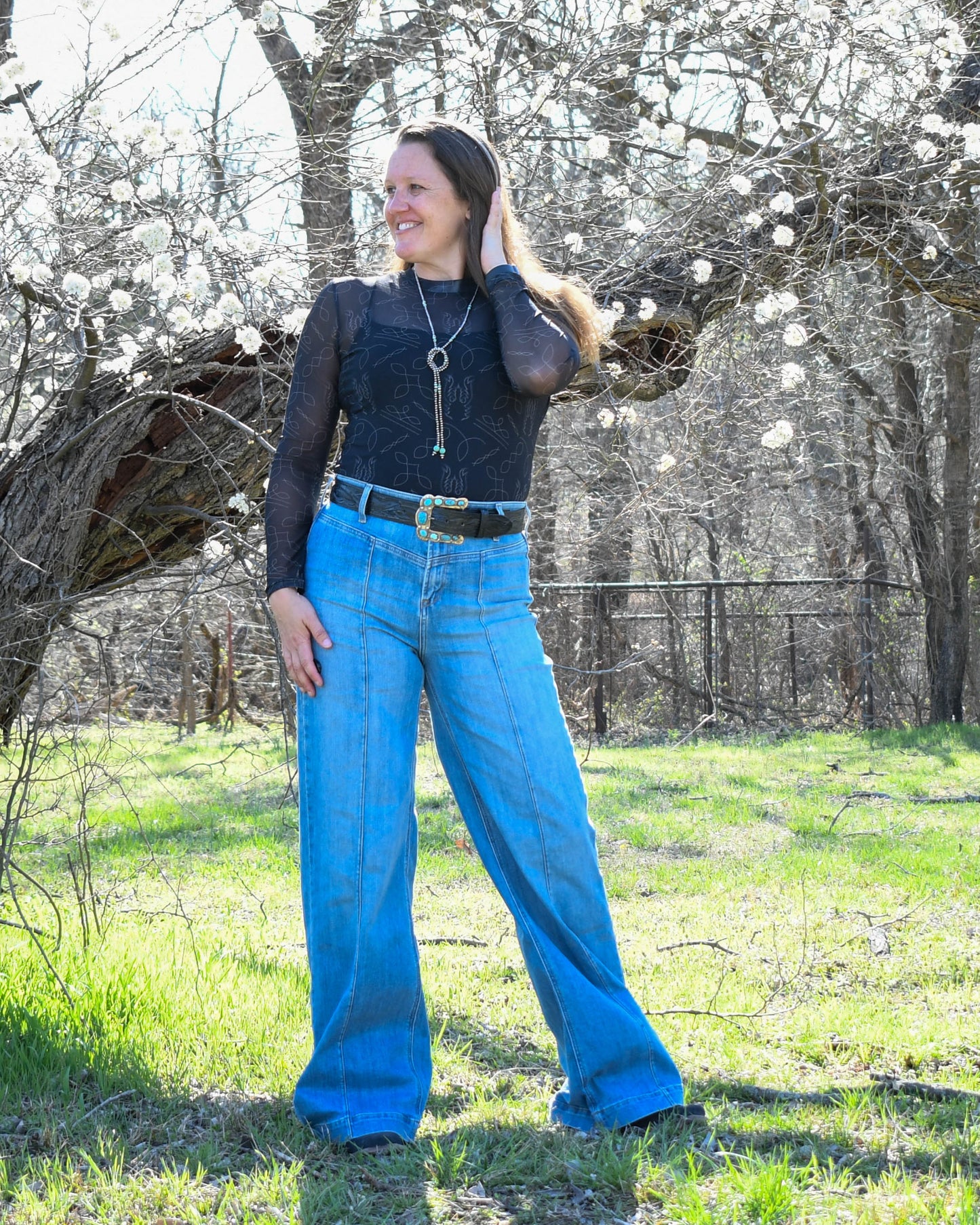 Model standing in wooded area wearing fashionable outfit with high waisted wide leg jeans