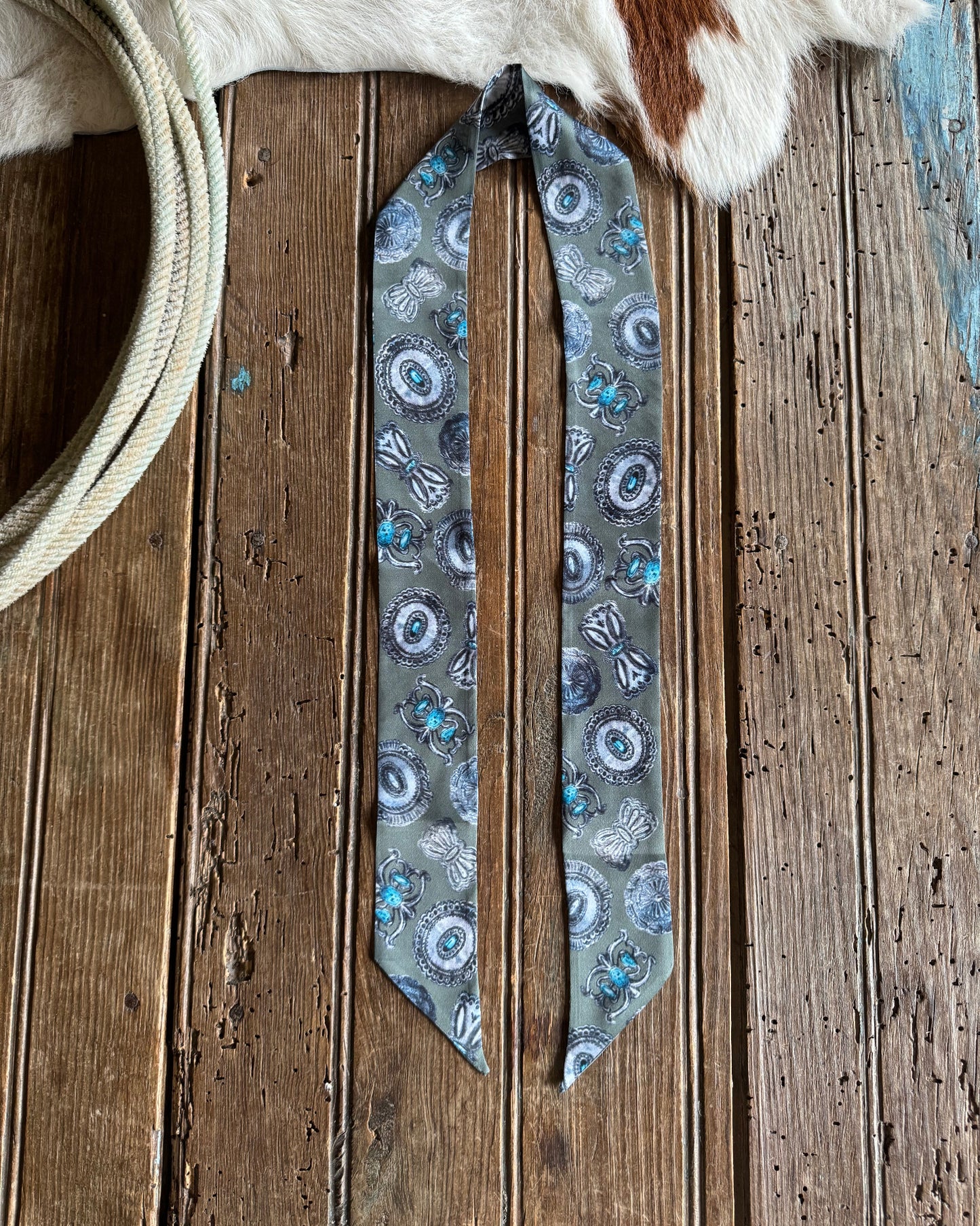 sage green ribbon scarf with turquoise concho pattern on a wooden surface