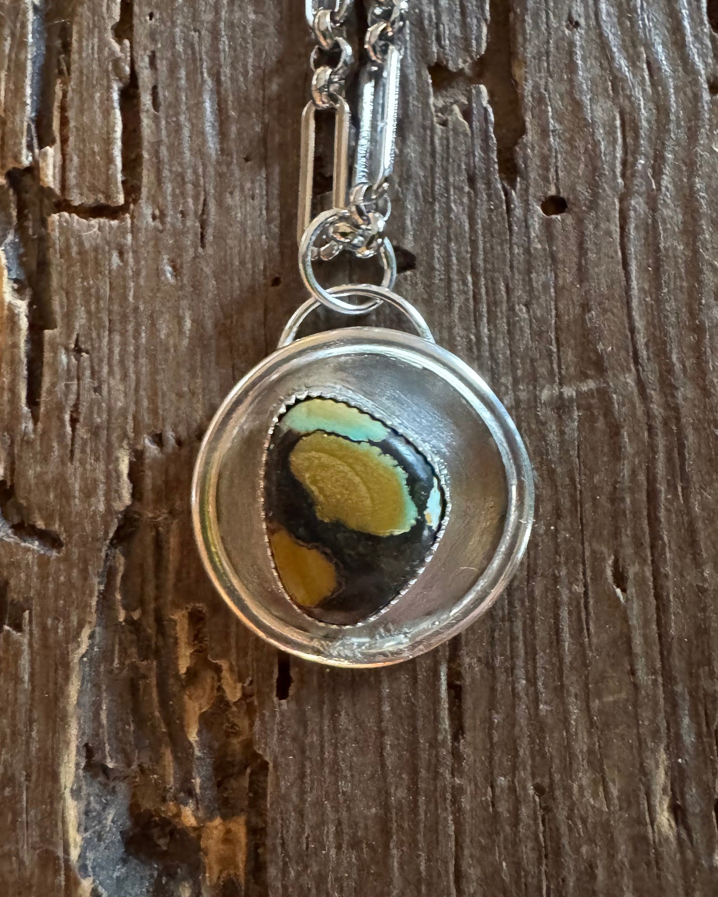 Silver pendant with a colorful stone on a wooden surface