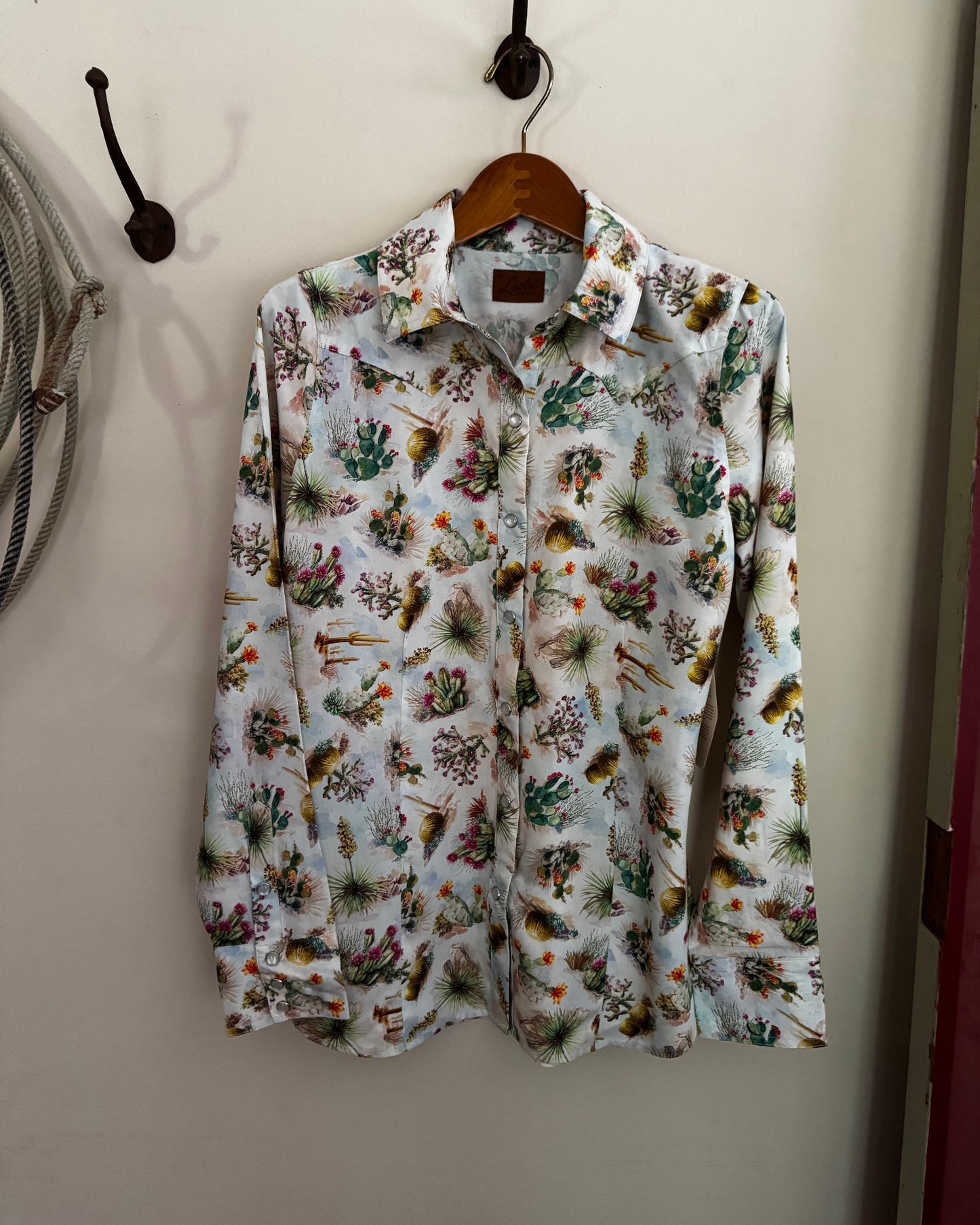 Floral patterned shirt hanging on a wooden hanger against a white wall.