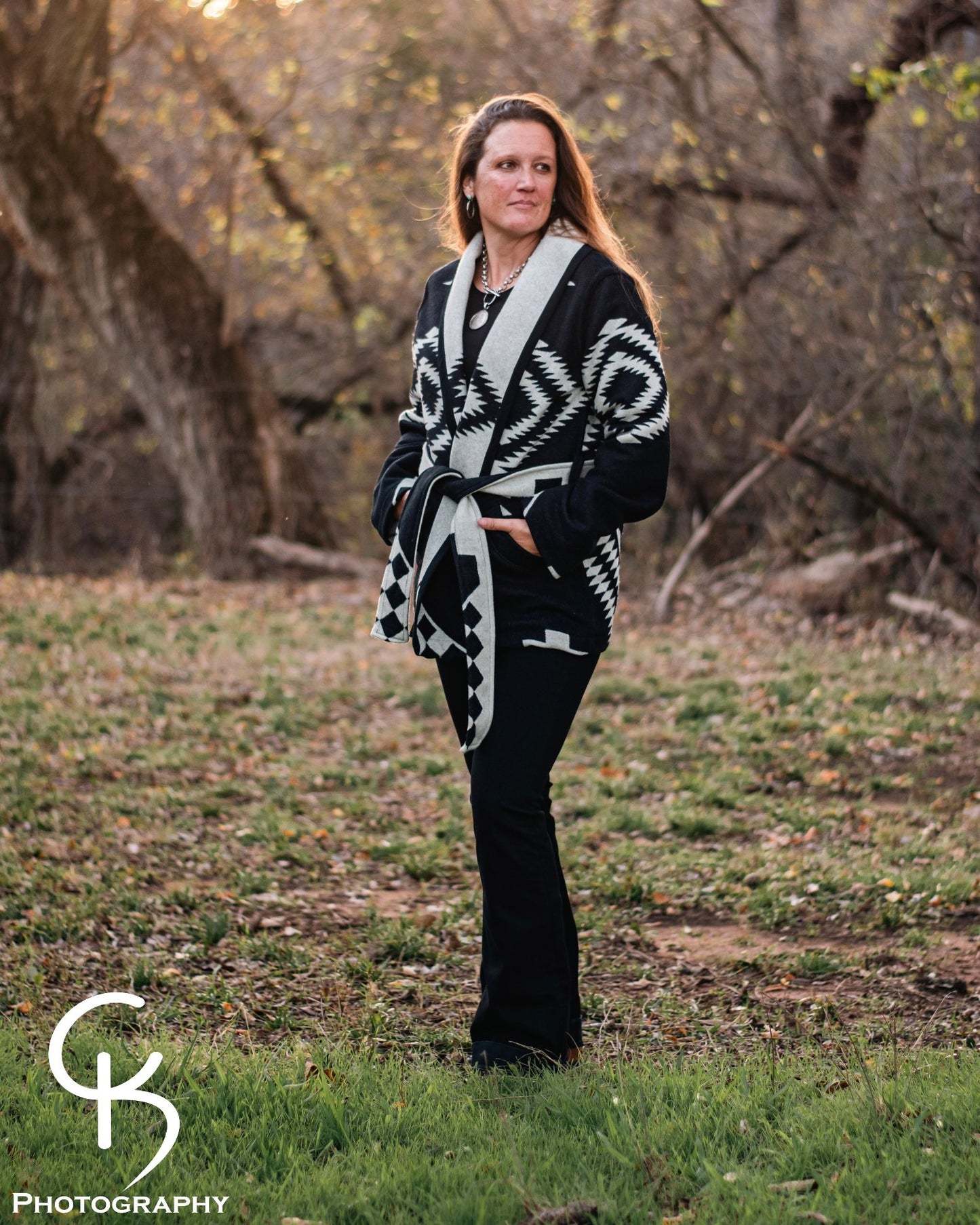 Model standing in a field wearing a Los Ojos Wrap Coat with bold southwestern patterns