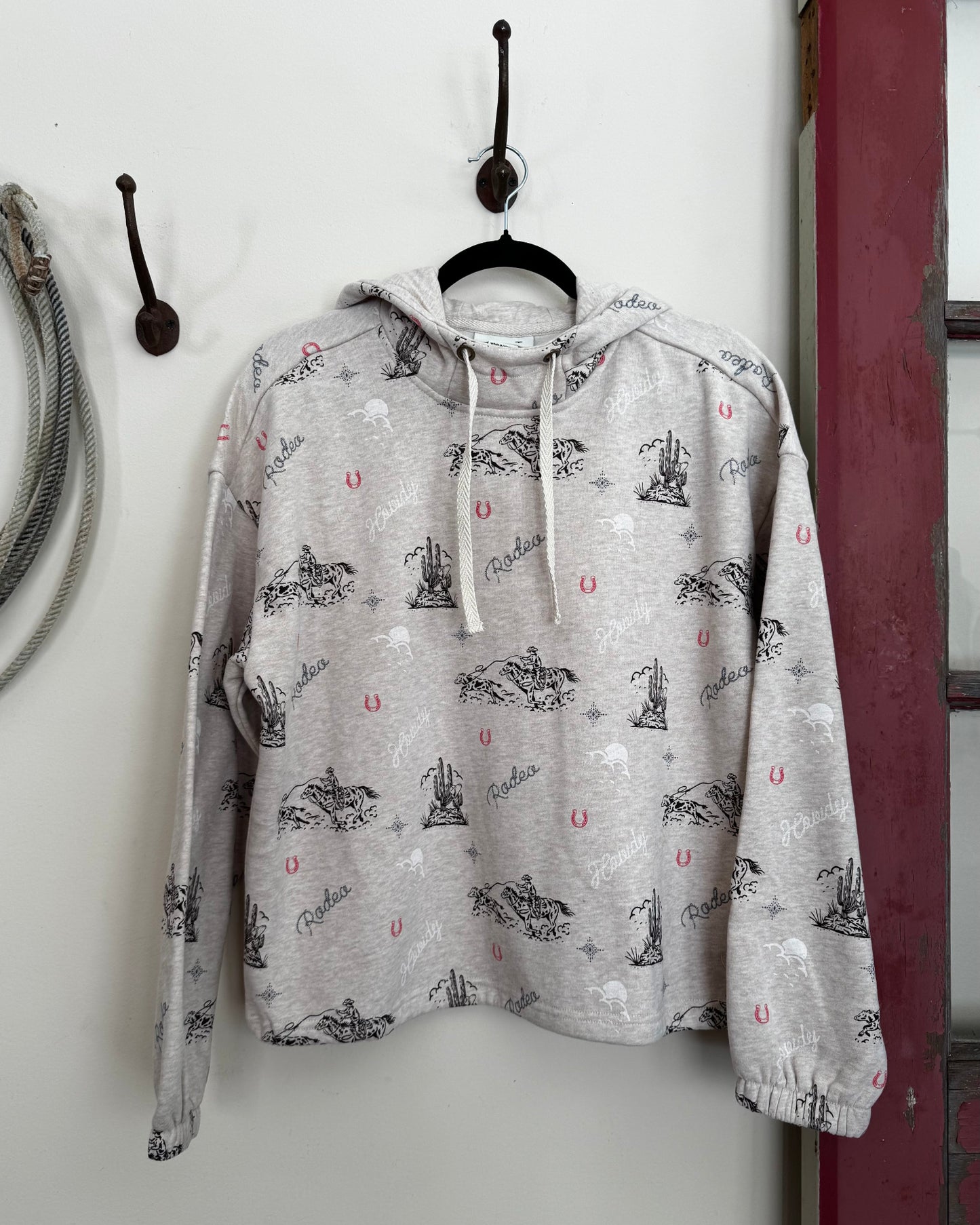 Oatmeal hoodie with black and red patterns hanging on a hook against a white wall.