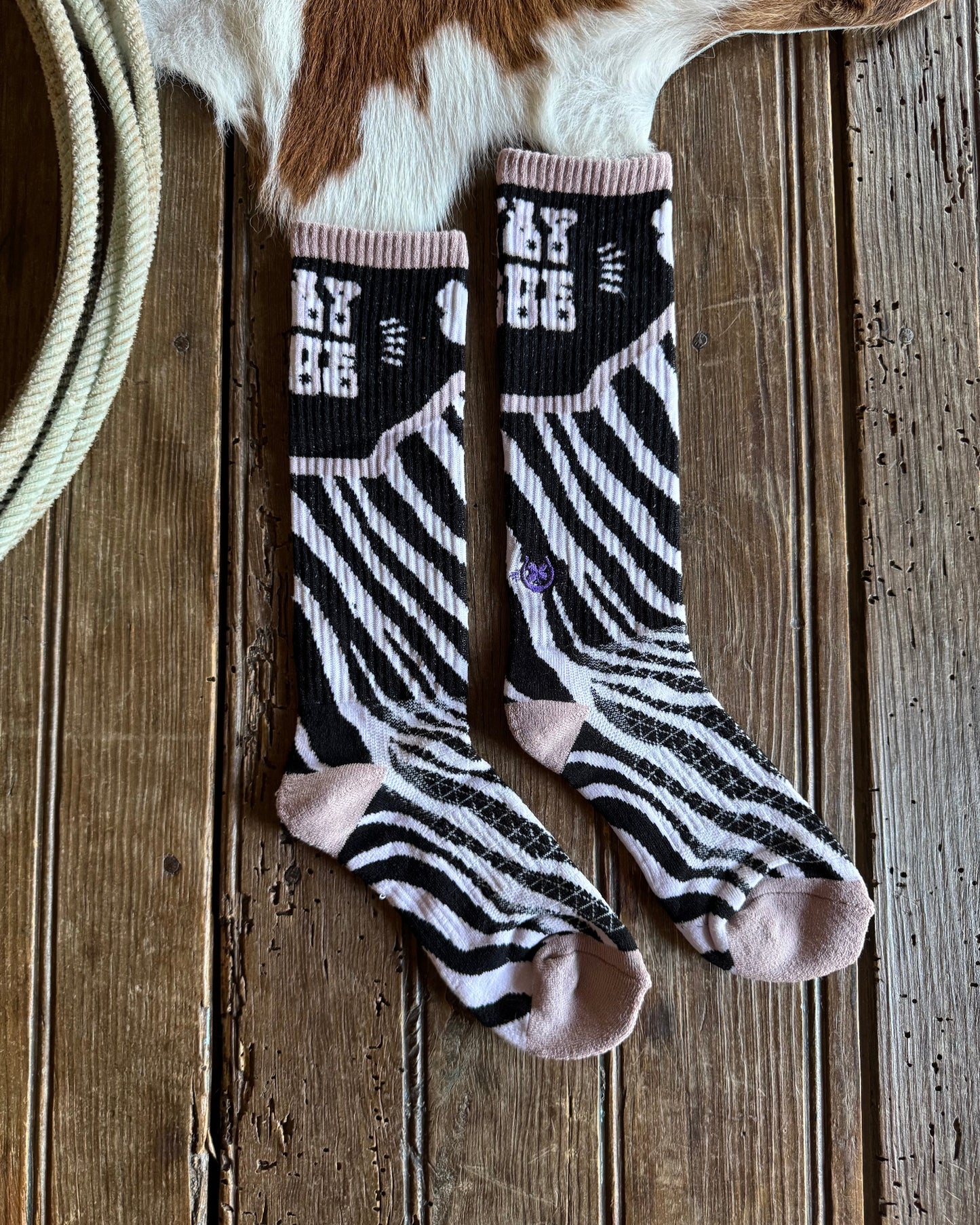 Pair of zebra-striped socks on a wooden surface with a cowhide rug in the background.