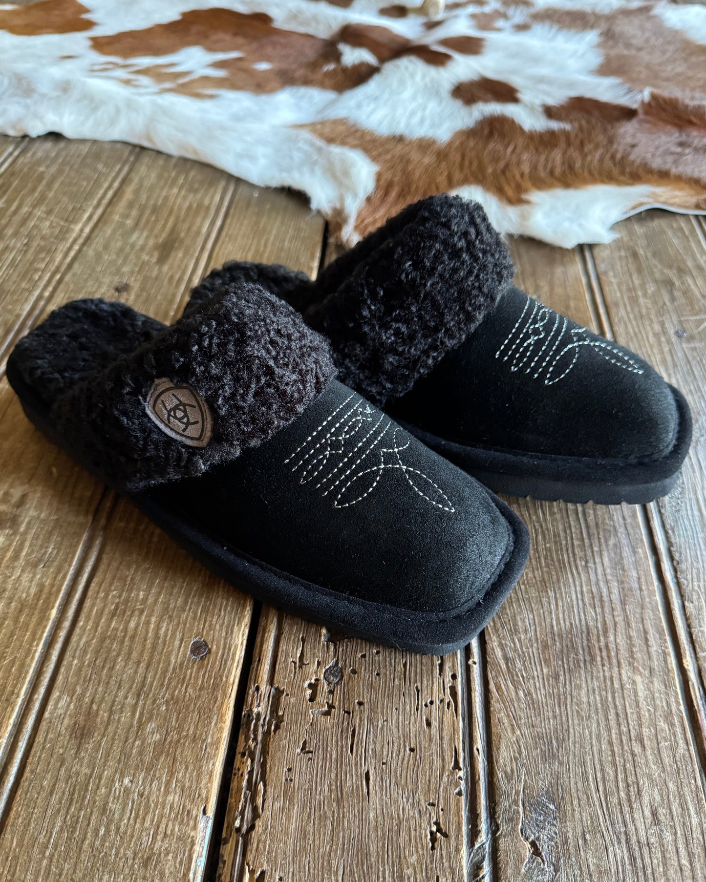 Black slippers with fuzzy texture on a wooden surface