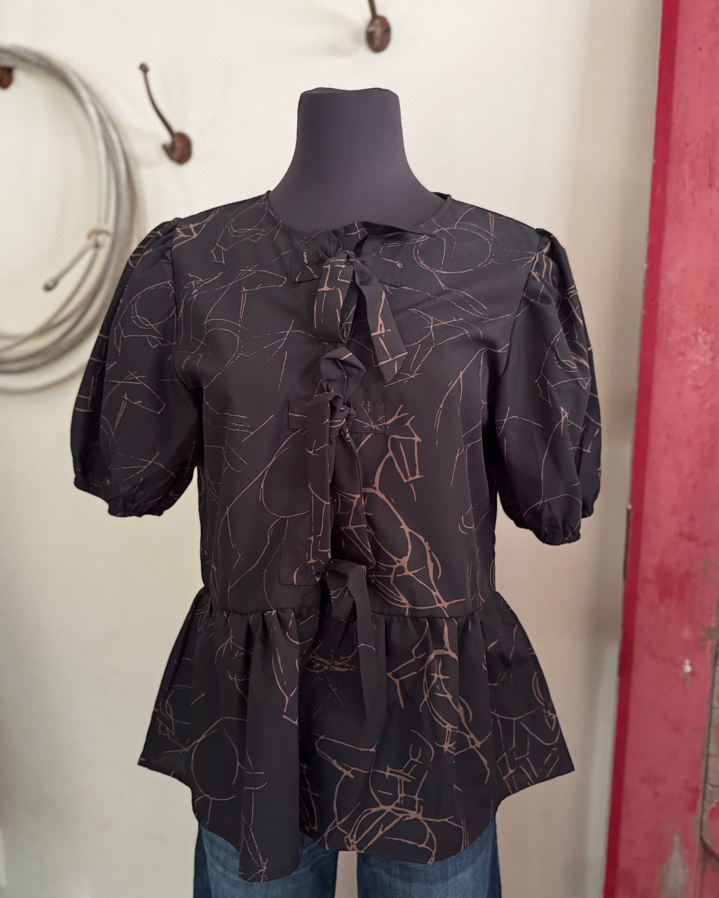 Black patterned blouse on a mannequin against a neutral wall.