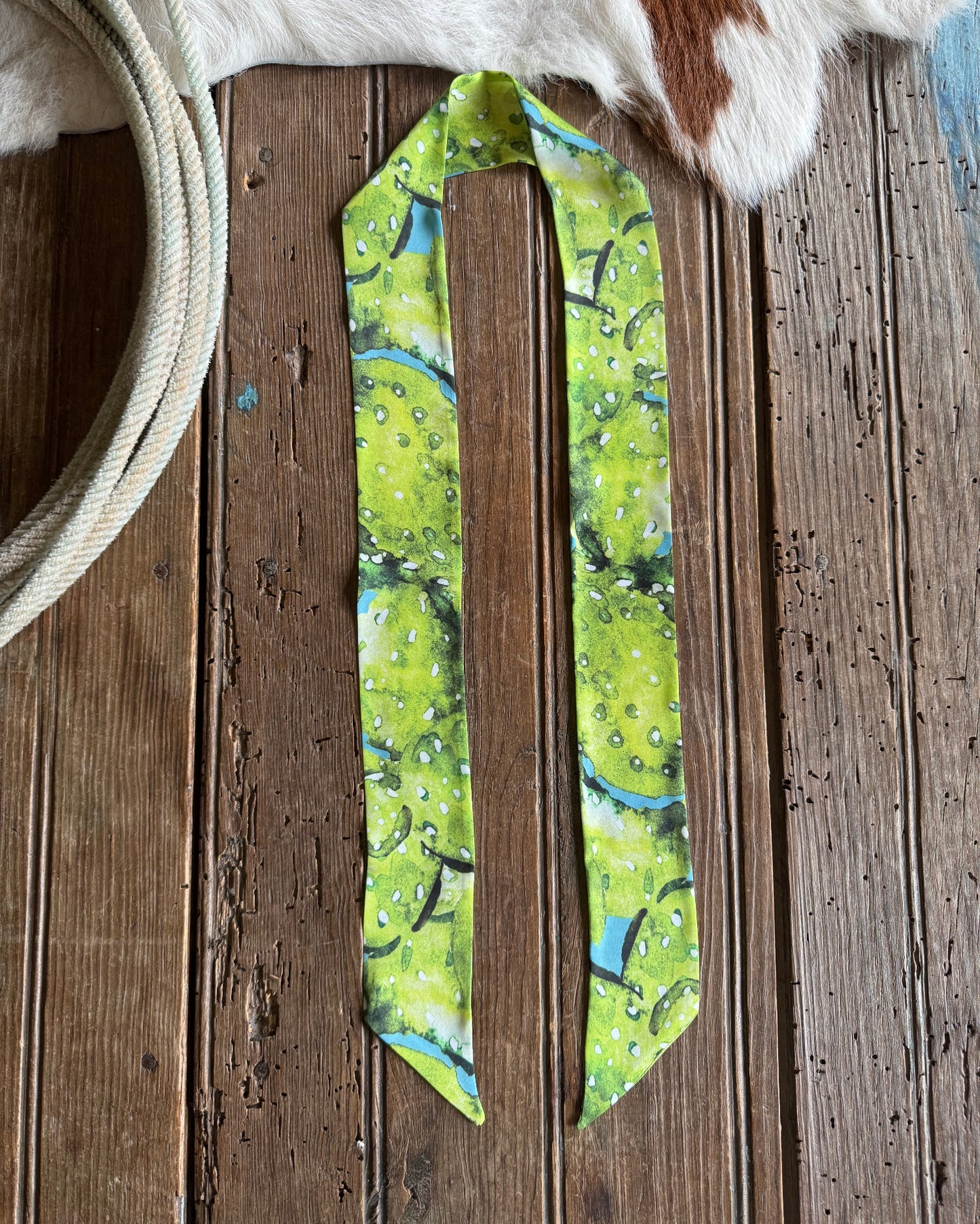 Green patterned cactus scarf on a wooden surface with cowhide leather and white rope.