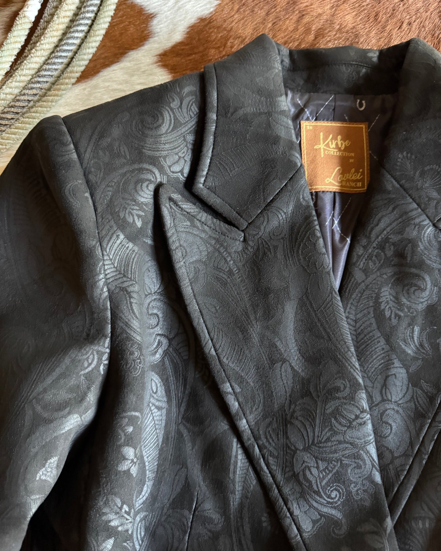 Close-up of a black paisley-patterned jacket with a brand tag on a horse.