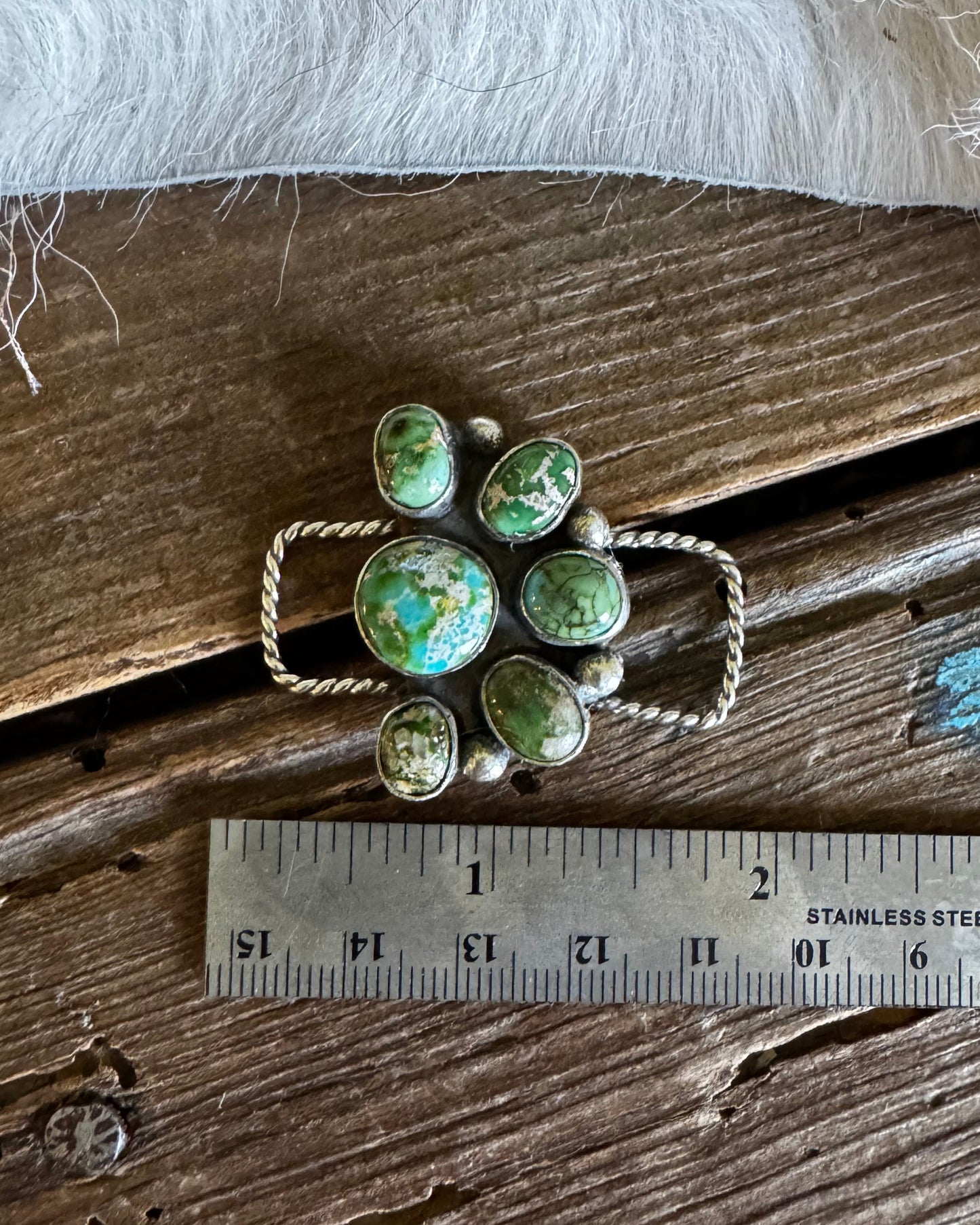 Green gemstone brooch on a wooden surface with a ruler for scale