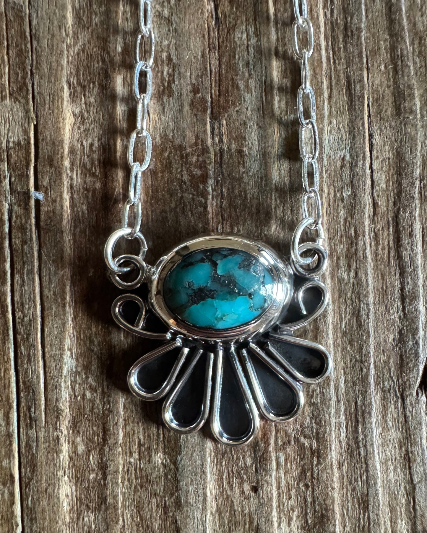 Close up of turquoise fan pendant on sterling silver necklace with rustic wood background