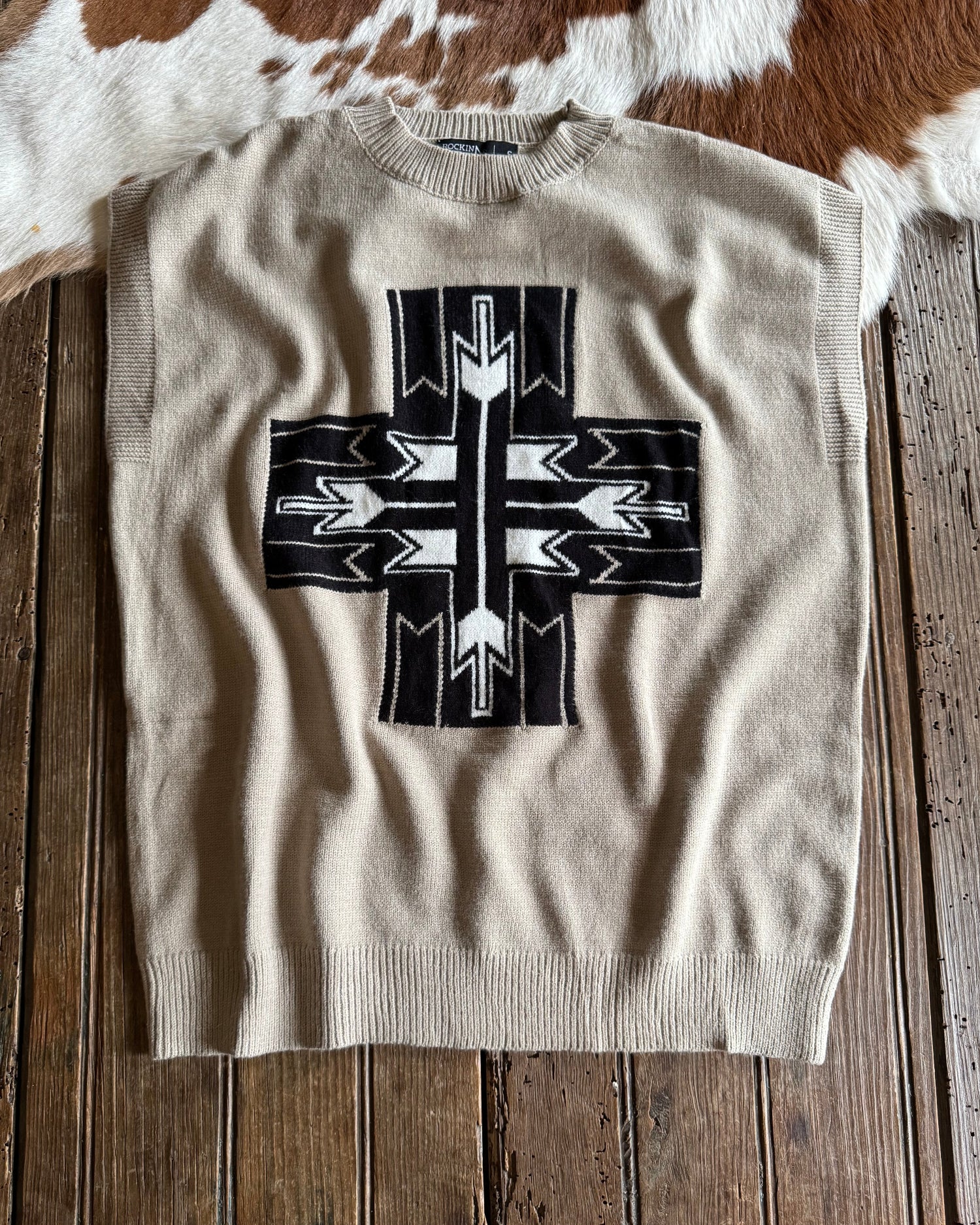 beige sweater vest with black and white arrow pattern on rustic wood background