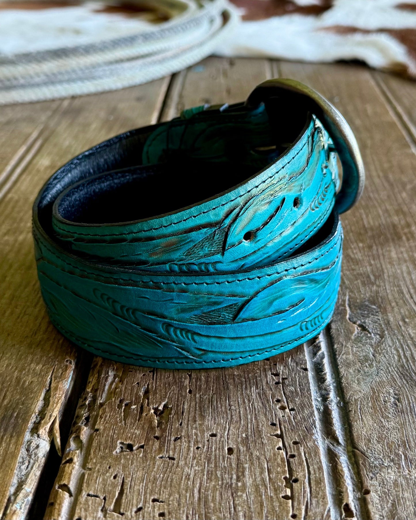 Turquoise leather belt with intricate designs on a wooden surface