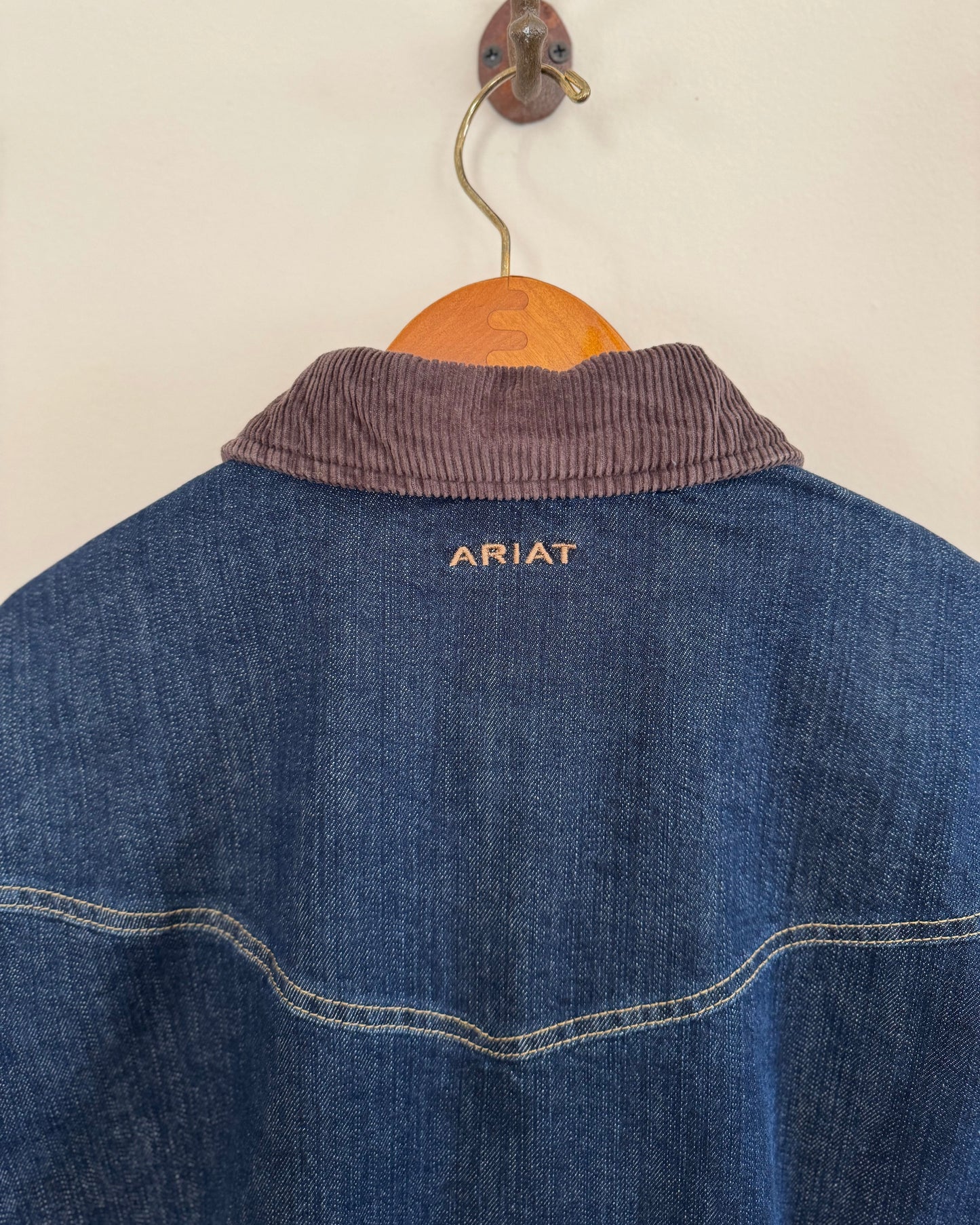 close up of back of men's denim jacket hanging on white wall