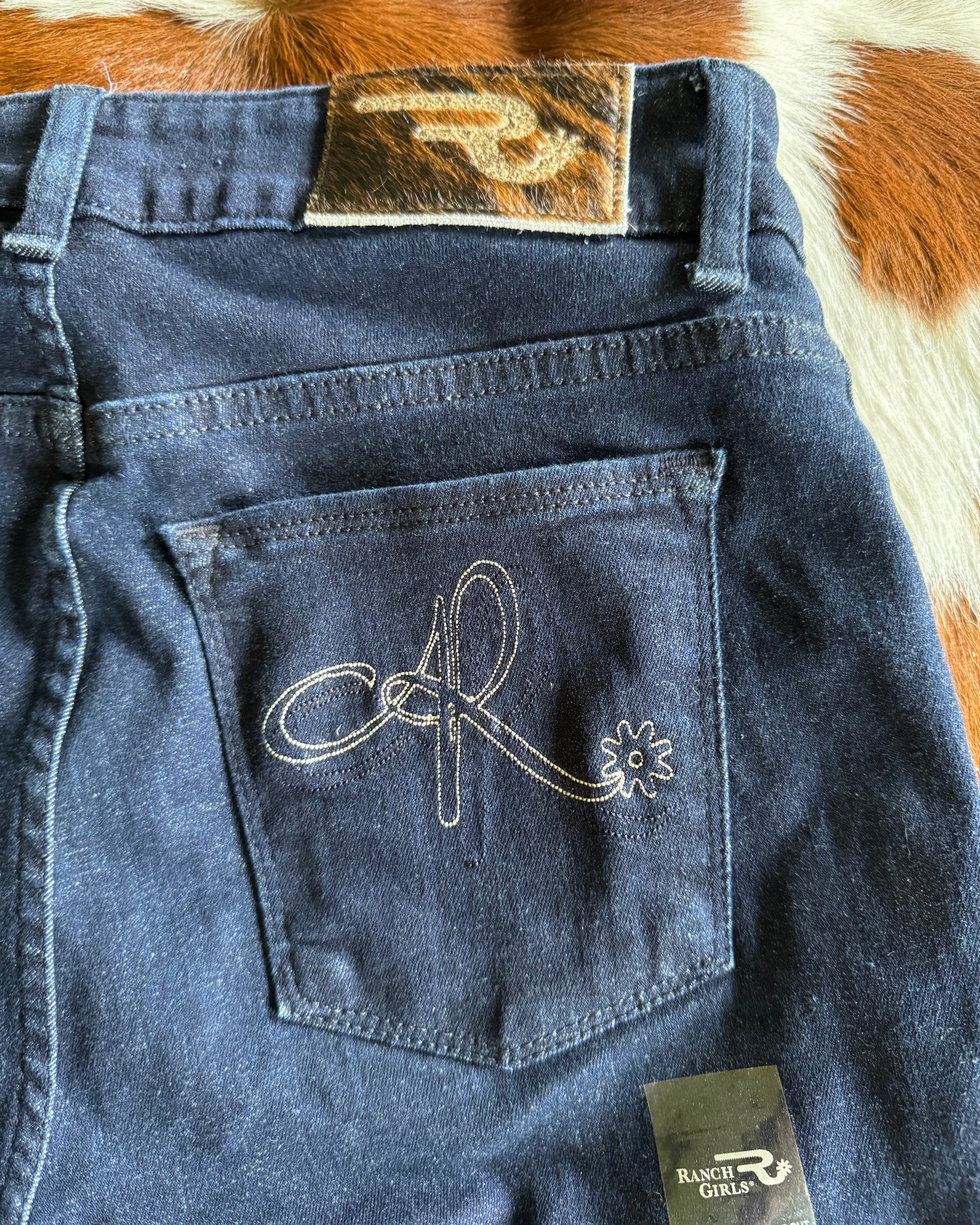 Blue denim jeans with a design on the pocket, displayed on a cowhide rug.