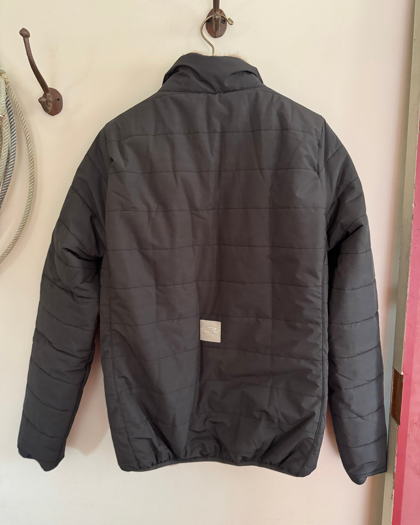 Dark gray quilted jacket hanging on a wall hook.
