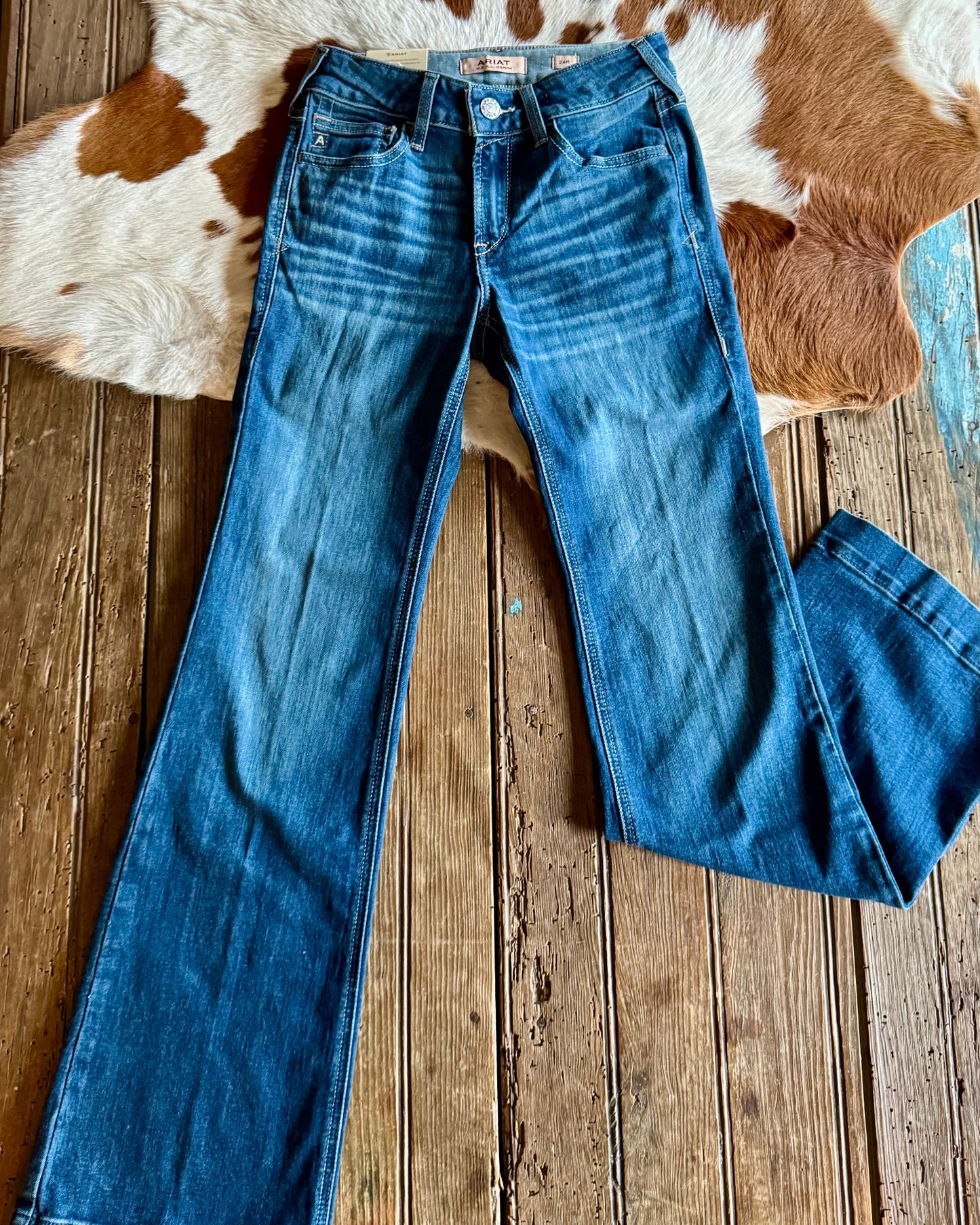 Blue jeans on a wooden floor with a cowhide rug in the background