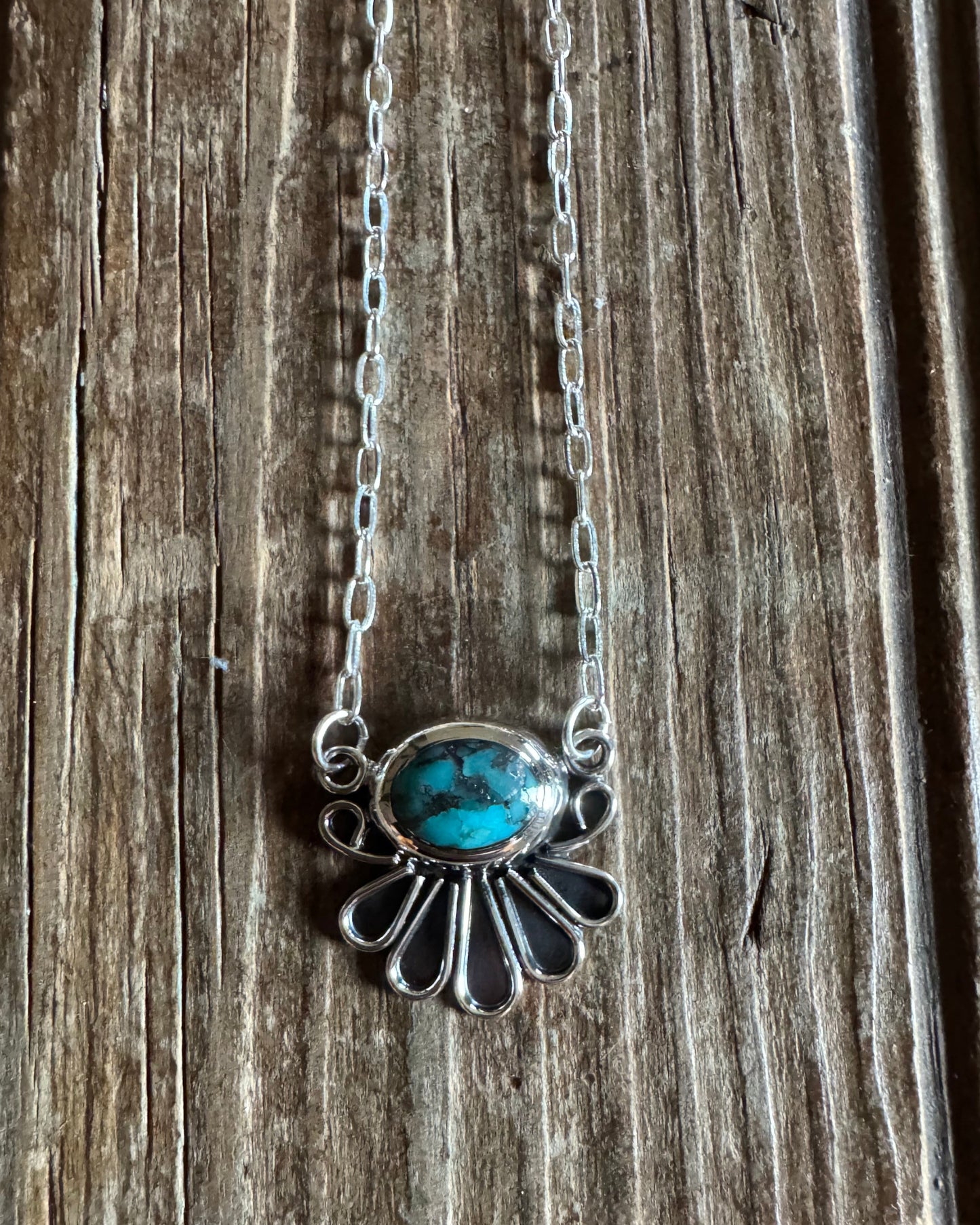 Sterling silver necklace with turquoise fan pendant on rustic wood background