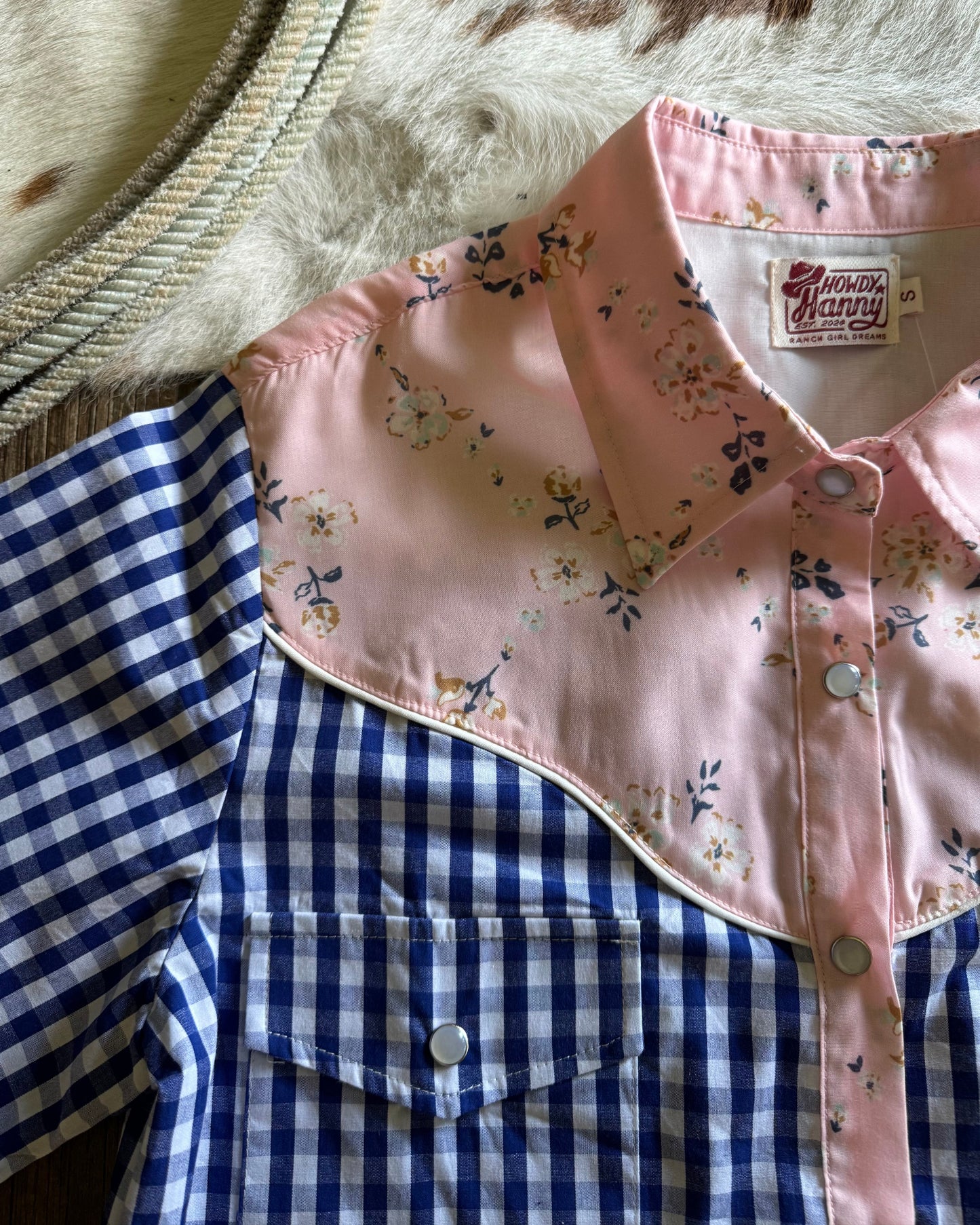 Pink floral shirt with blue plaid shirt underneath on a textured surface