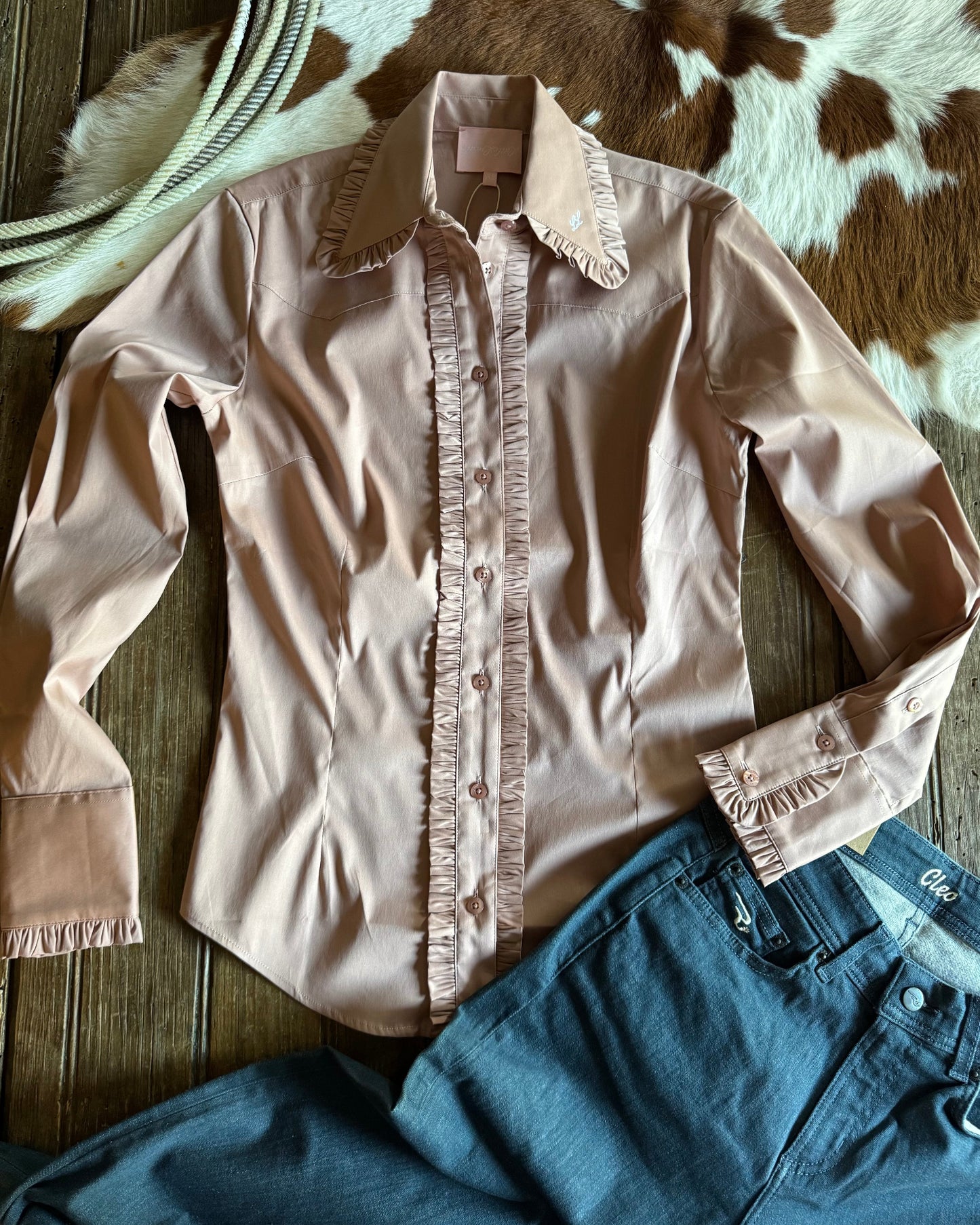 Light pink blouse with ruffled details on a wooden surface with denim pants.