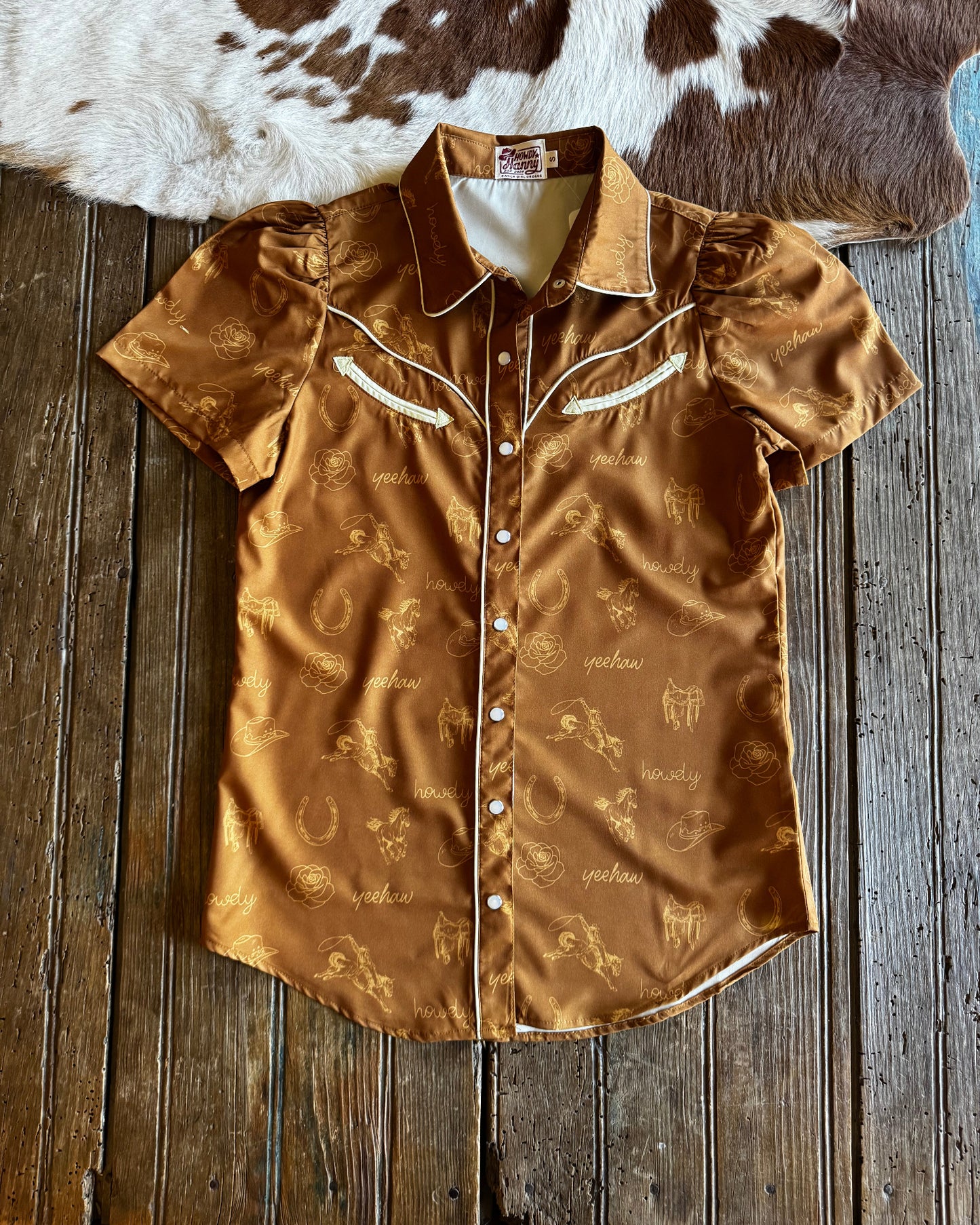 Brown patterned garment on a wooden surface next to a cowhide rug