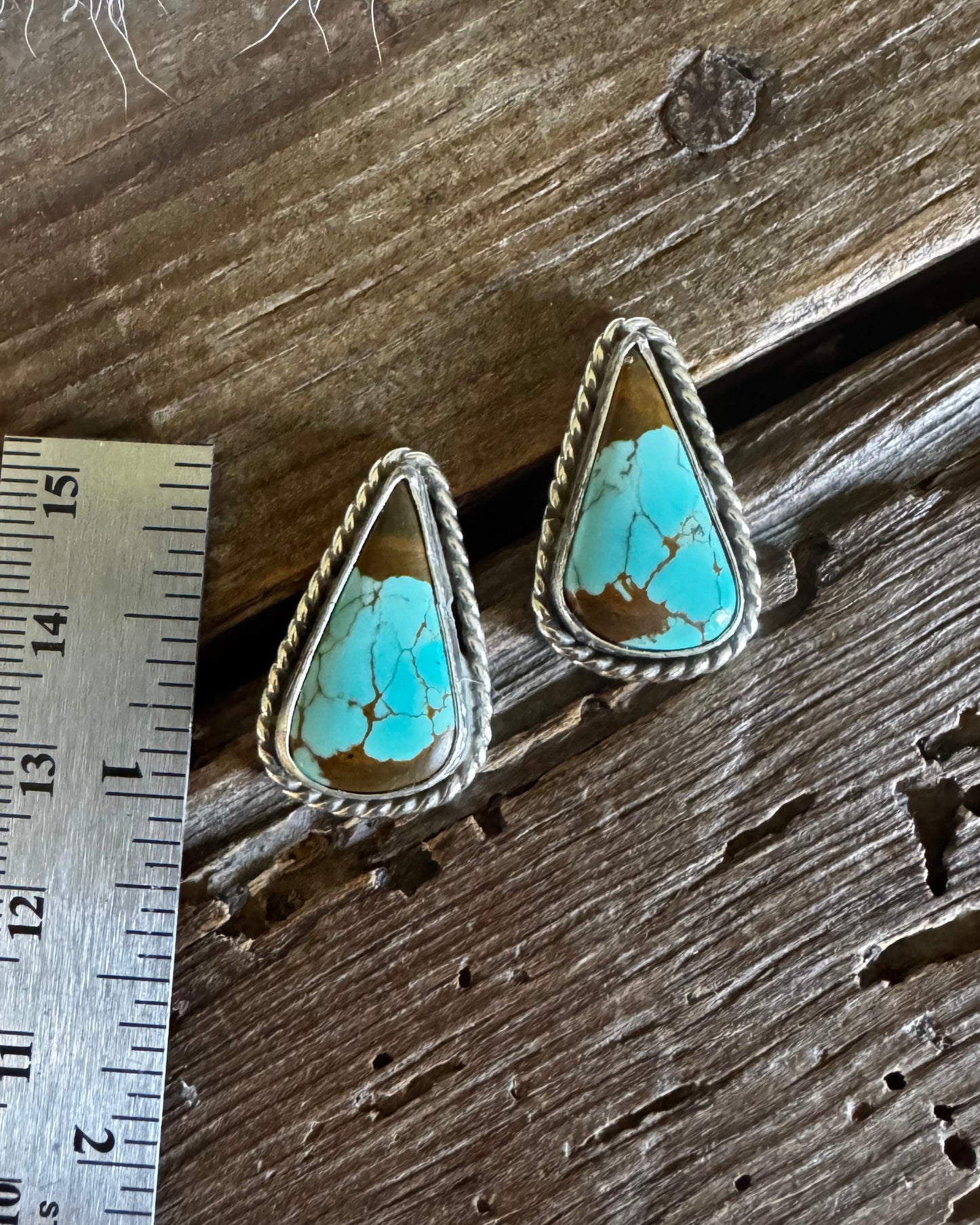 Turquoise stone earrings on a wooden surface with a ruler for scale.