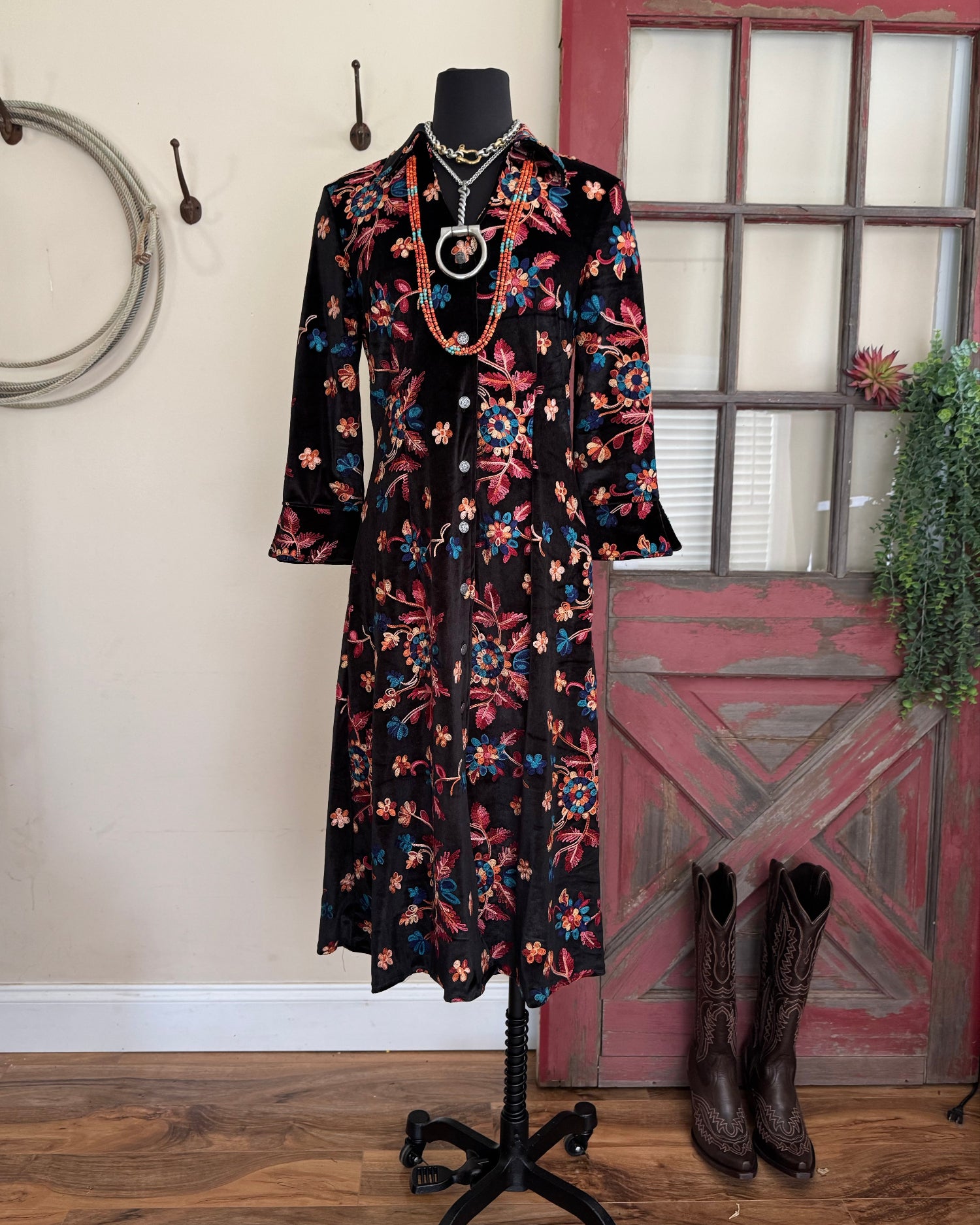 Floral dress on a mannequin with boots on a wooden floor against a rustic wall.