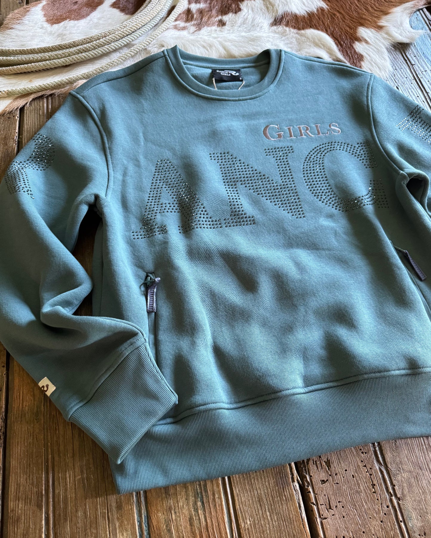 Blue sweatshirt with 'RANCH GIRLS' text on a wooden surface