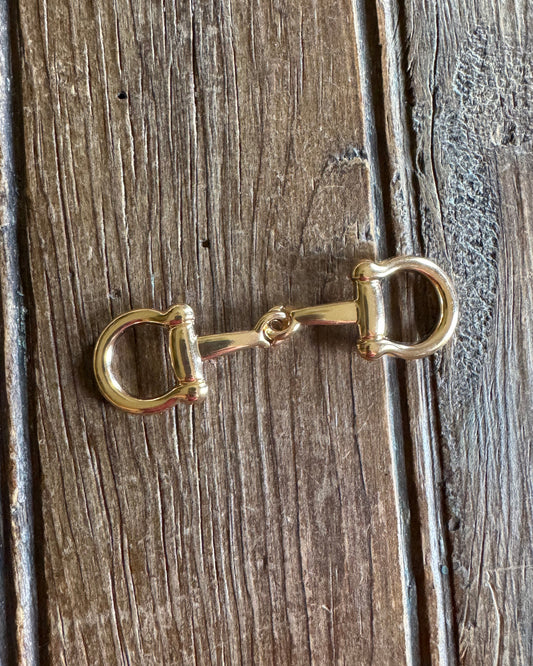 Gold horse bit charm on a wooden surface