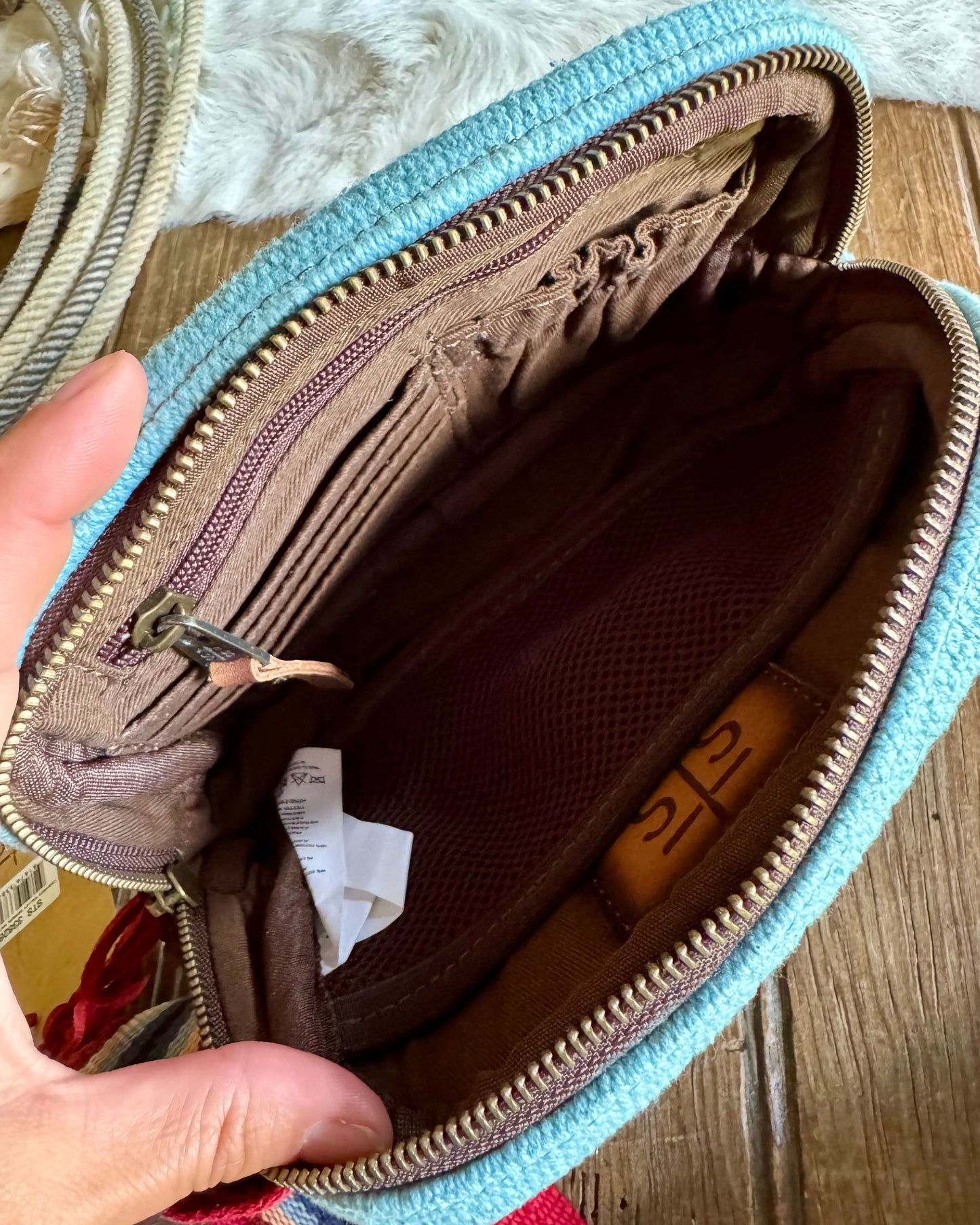 Open blue and brown pouch with a hand holding it, on a wooden surface.