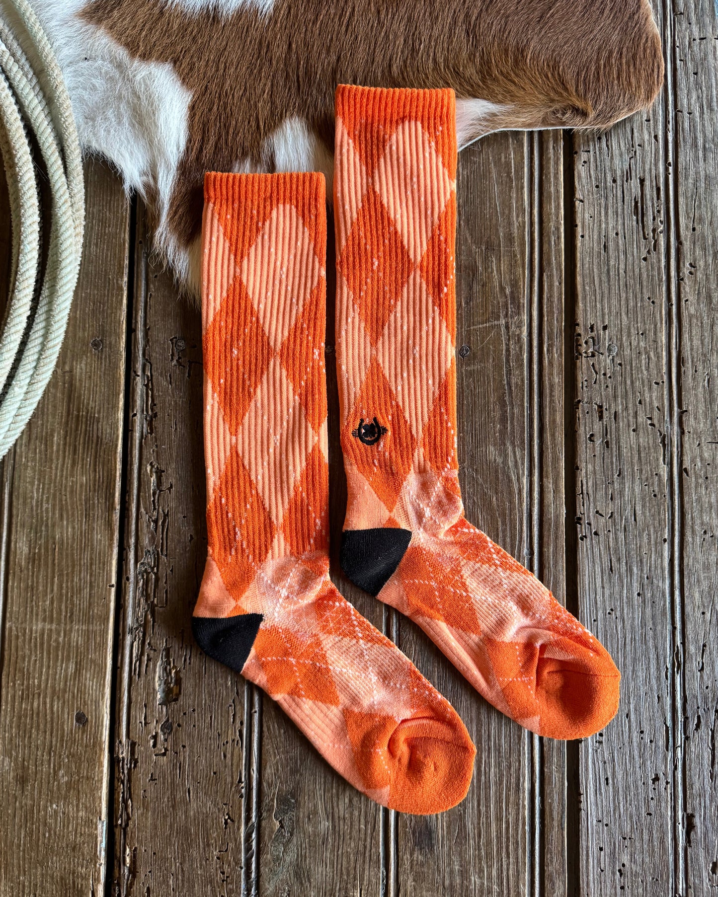 Orange patterned socks on a wooden surface with a cow and rope in the background