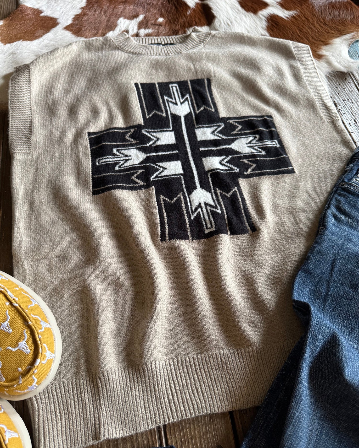 beige sweater vest with arrow cross on rustic wood background with cowhide