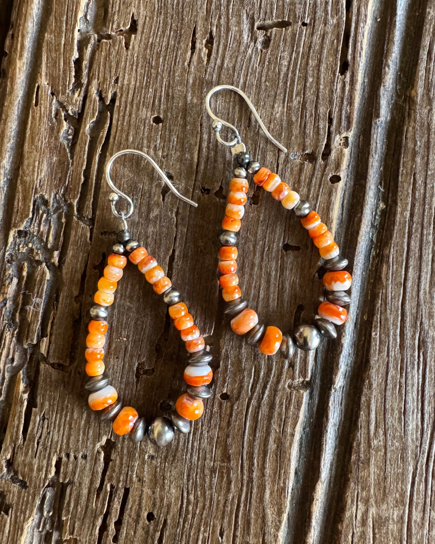 Orange spiny loop earrings with sterling silver pearls on rustic wood background