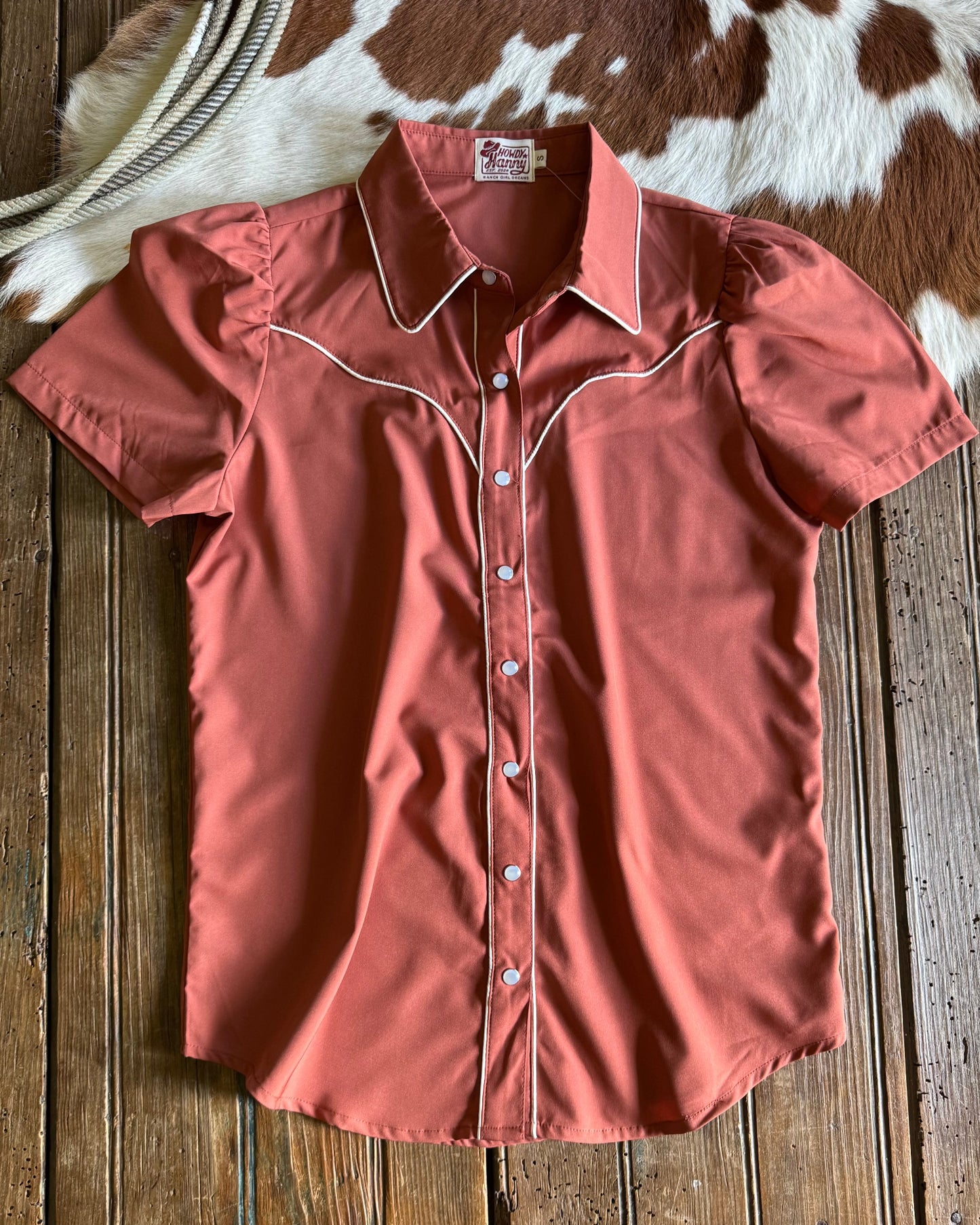 rust short-sleeve shirt with white trim on a wooden surface with cowhide rug