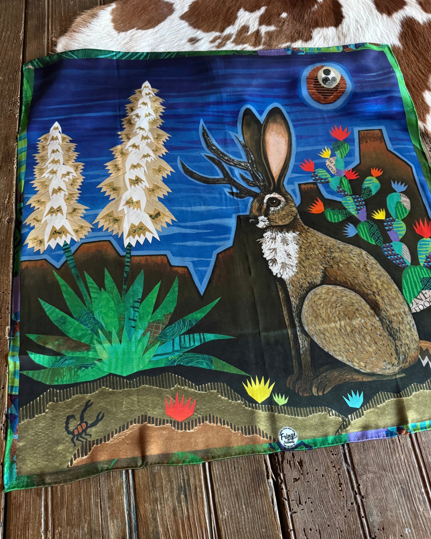 Scarf with a colorful design of a jackalope and nature elements on a wooden surface.