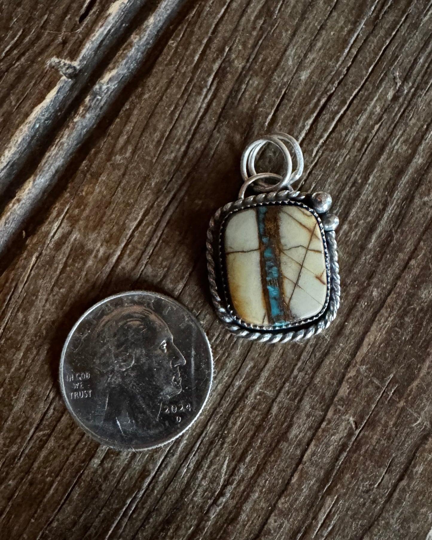 Silver pendant with a stone on a wooden surface next to a coin for scale.