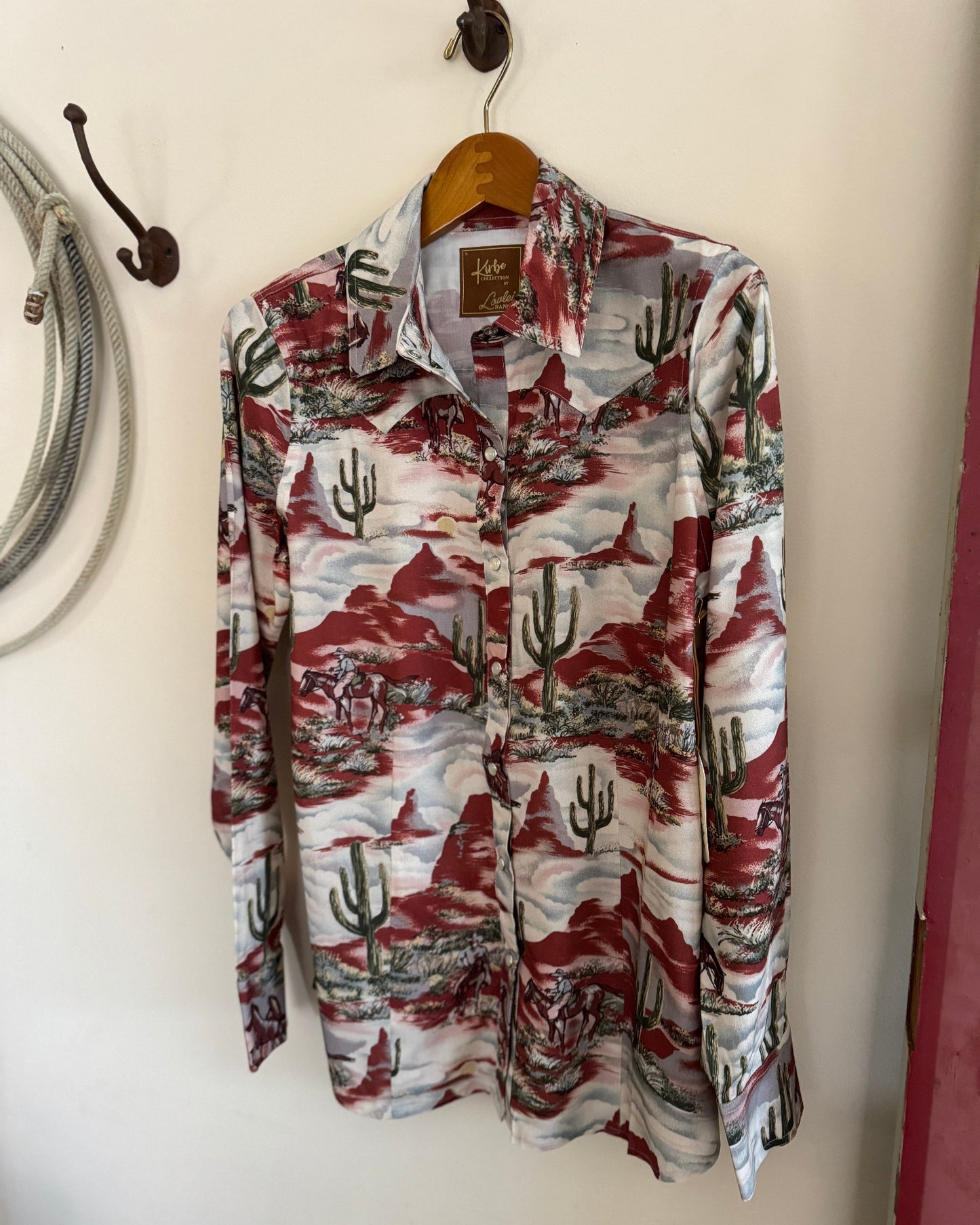 Long-sleeve shirt with nature-themed pattern on a hanger against a white wall.