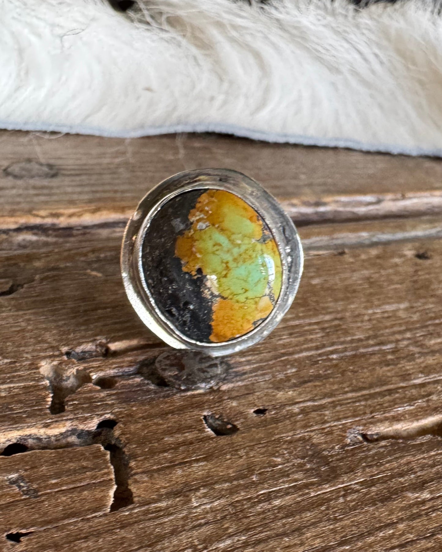 A round clear resin ring holder or coaster featuring a split design of vibrant orange-yellow and dark black, resting on a rustic wooden surface.