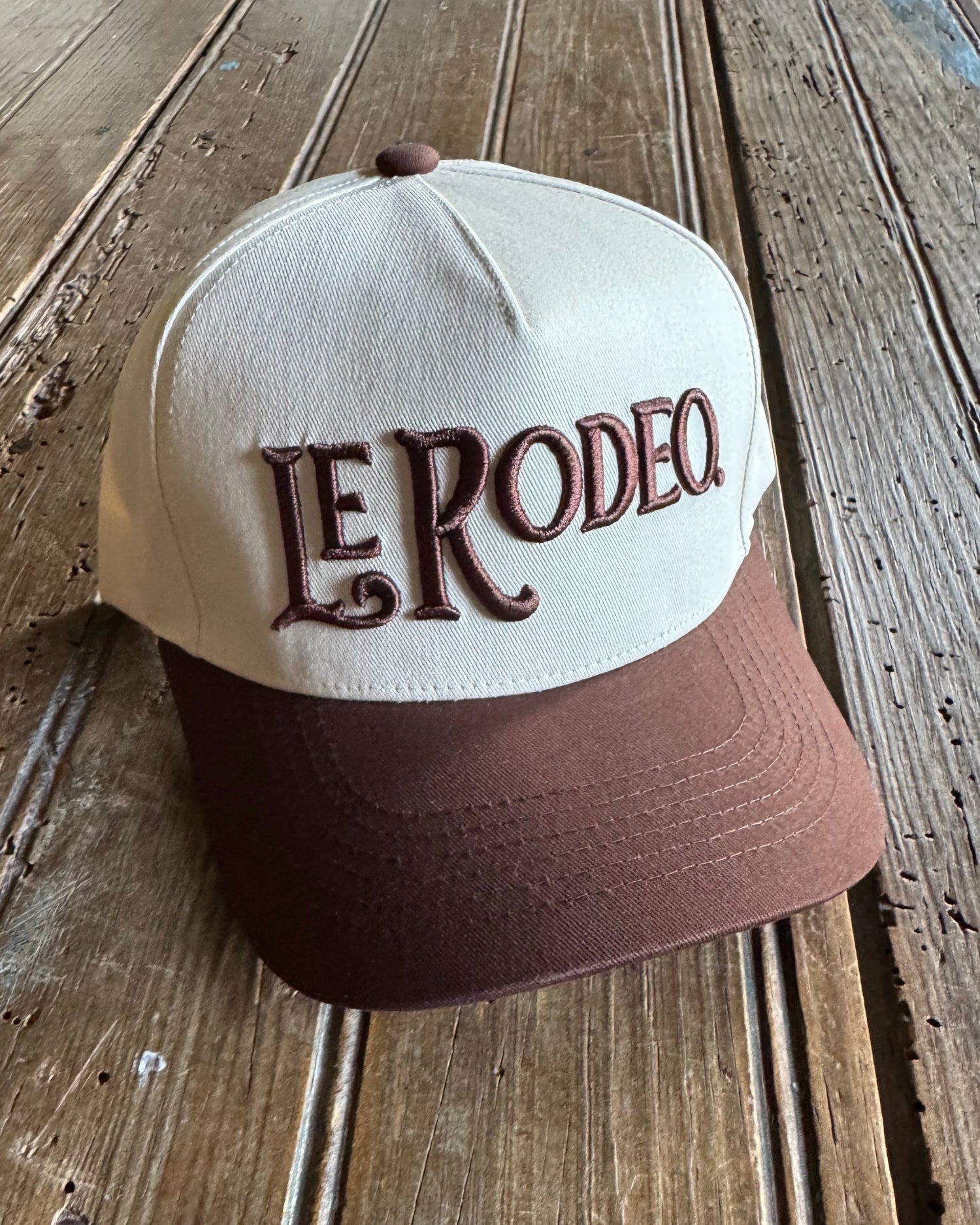 Brown and white cap with 'Le Rodeo' branding on a wooden surface
