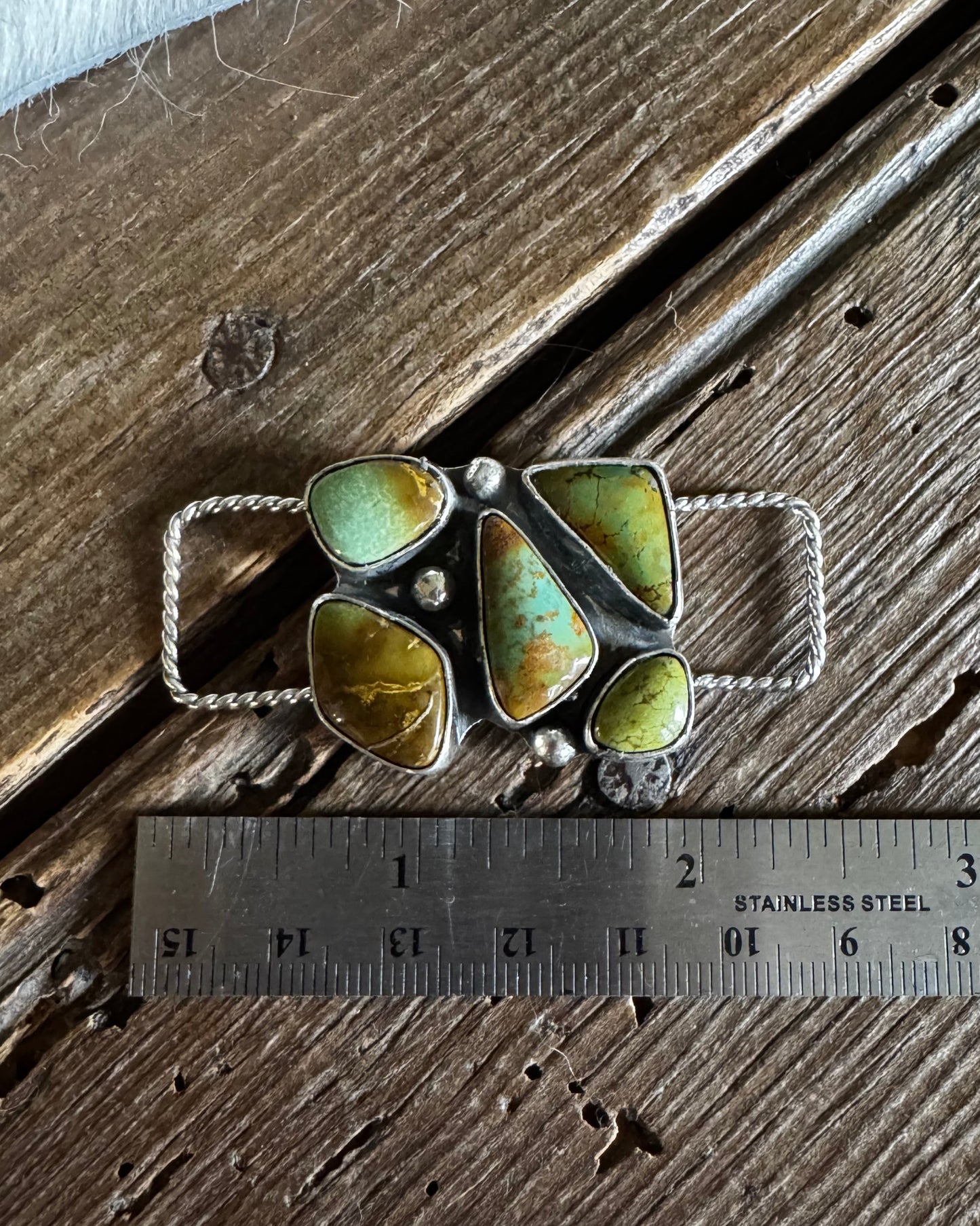 Jewelry piece with green stones on a wooden surface next to a ruler for scale.