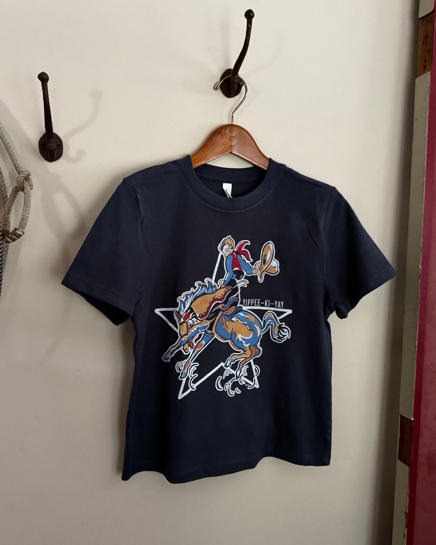 Navy blue t-shirt with graphic design on a wooden hanger against a white wall.