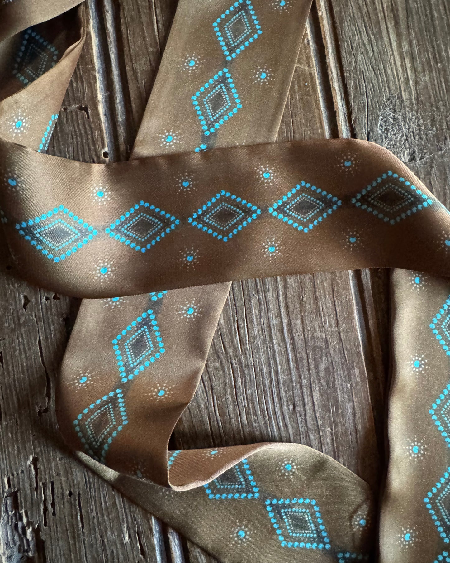 Brown ribbon scarf with blue geometric pattern on a wooden surface