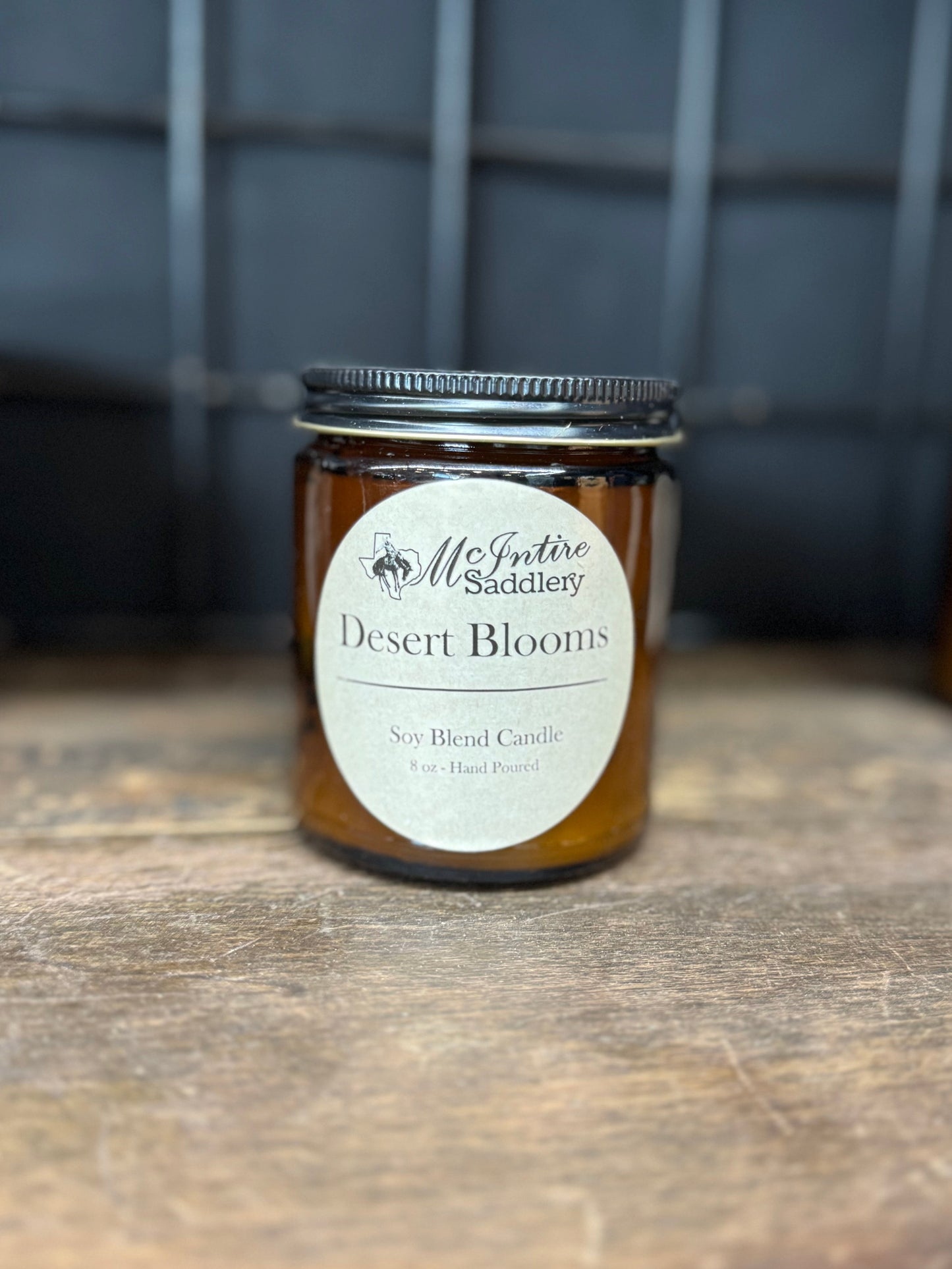 Jar of 'Desert Blooms' candle with a label on a wooden surface