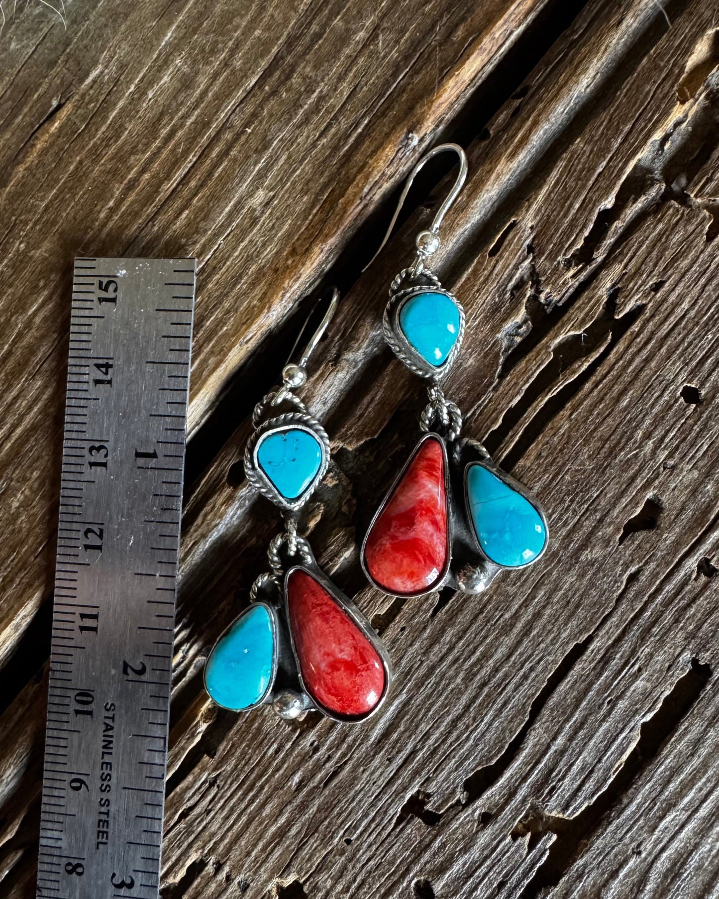 Pair of earrings with turquoise and red stones on a wooden surface with a ruler for scale.