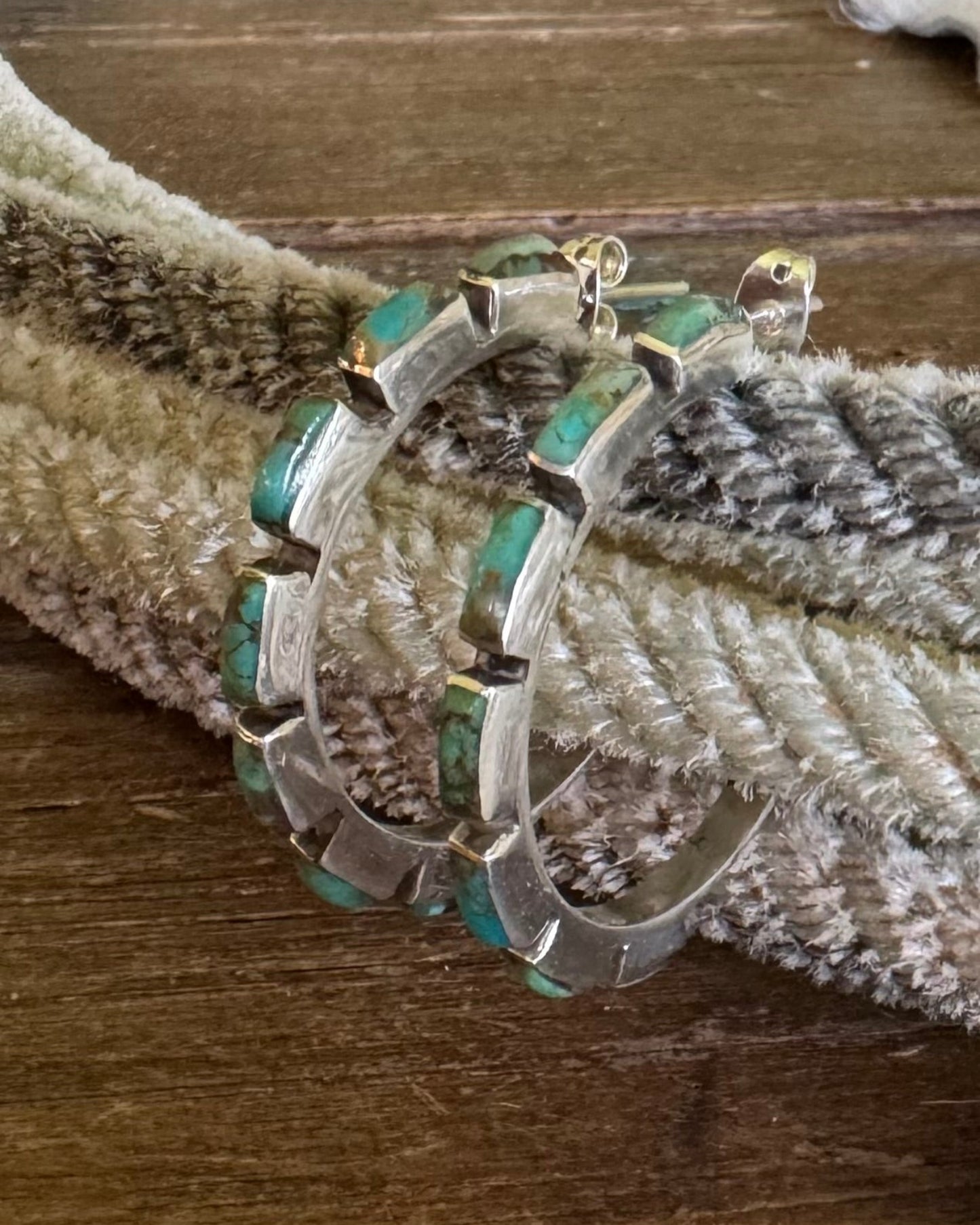 Silver hoop earrings with turquoise stones on a textured surface