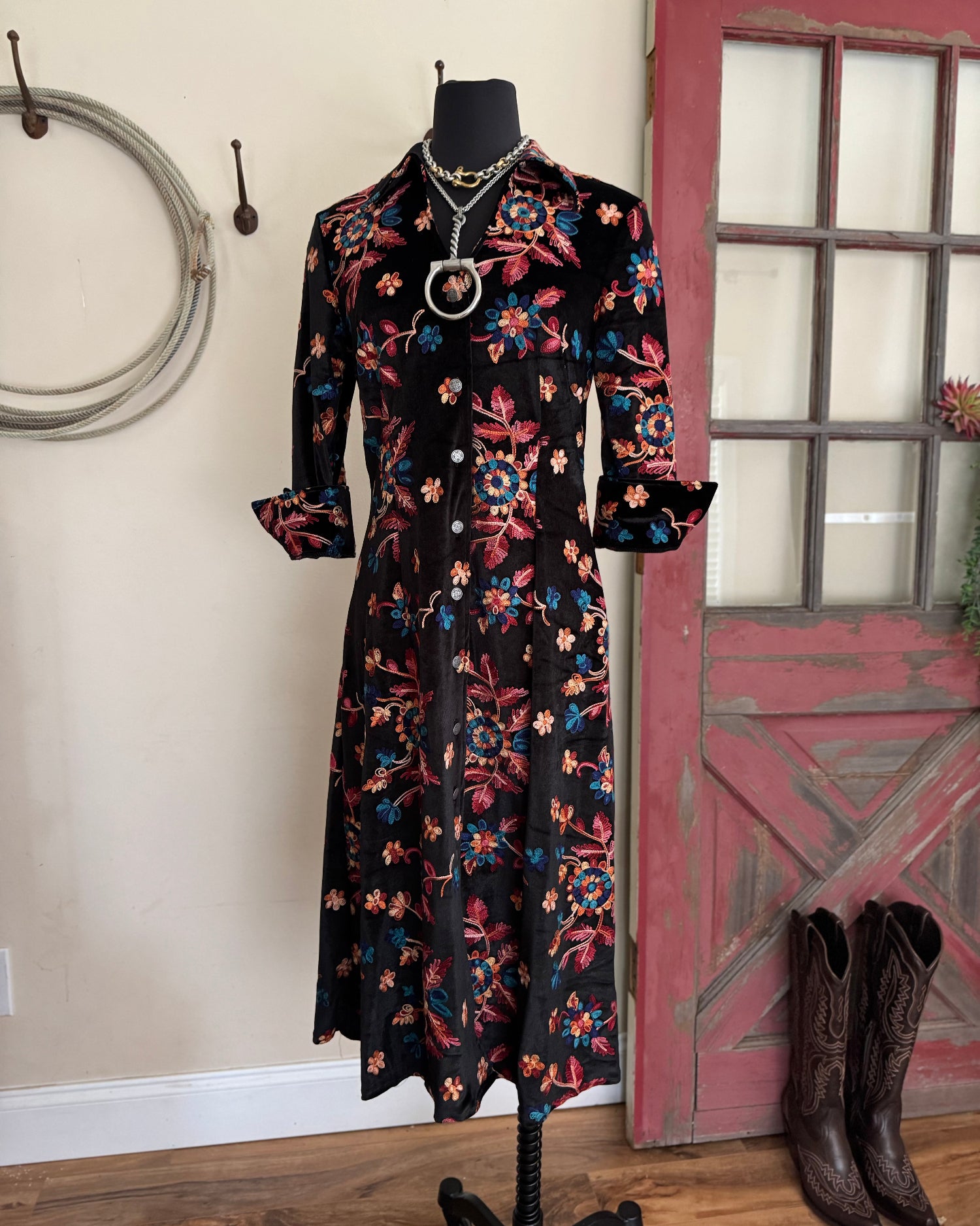 Floral dress on a mannequin with cowboy boots on a wooden floor.