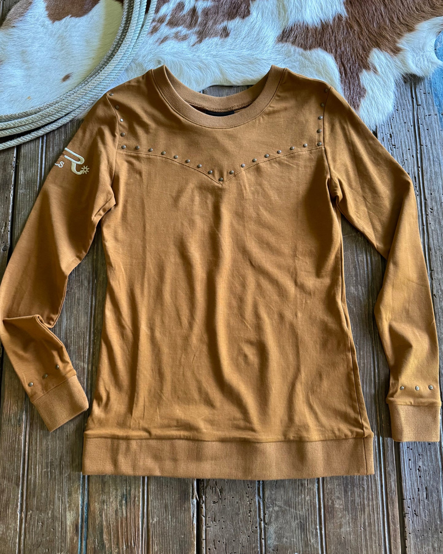 Brown long-sleeve shirt on a wooden surface with a cowhide rug in the background