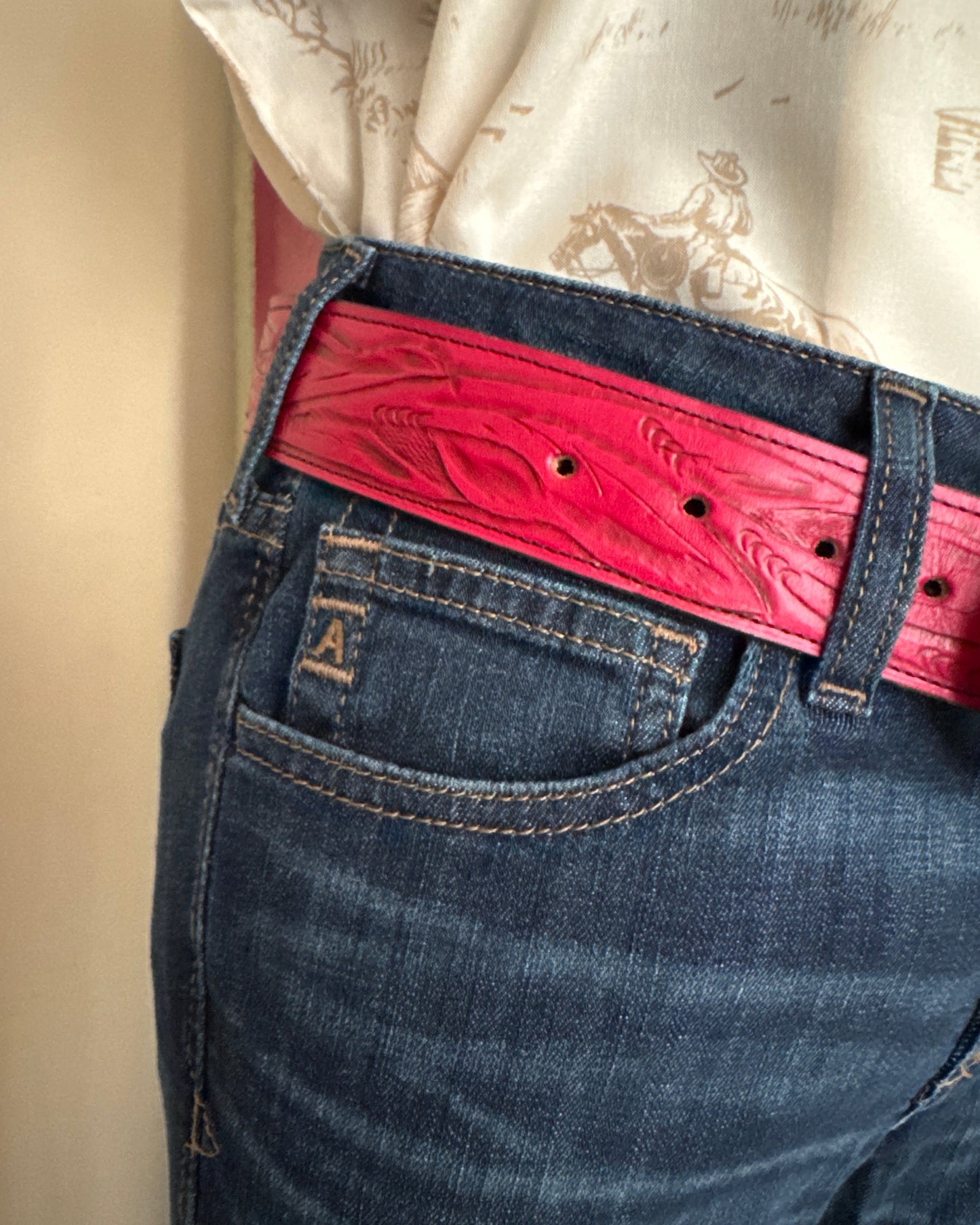 Close-up of blue jeans with a red belt and white lace garment.