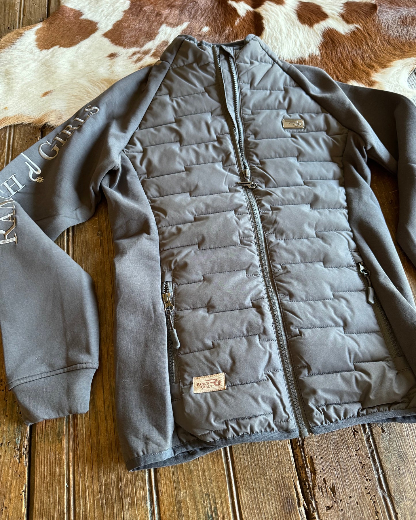 Gray quilted jacket on a wooden surface with a cowhide rug
