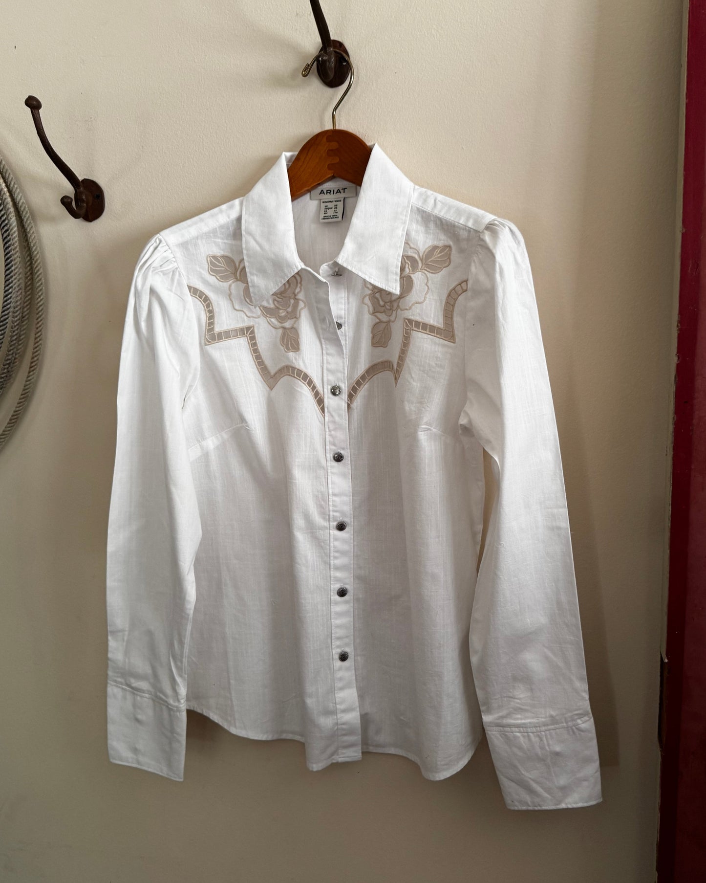 White shirt with lace details on a hanger against a beige wall.