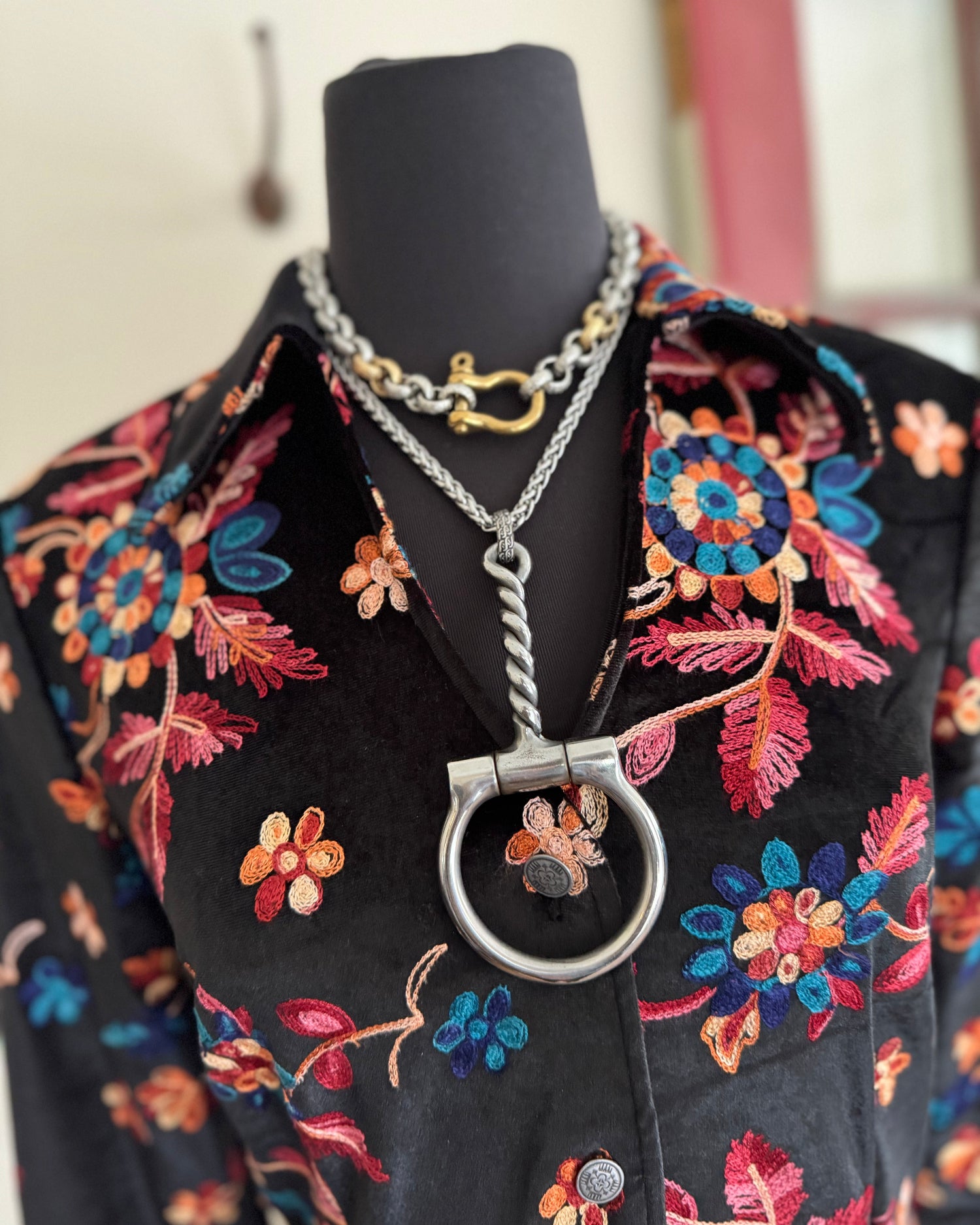 Necklace with a large silver clasp on a black mannequin wearing a floral-patterned garment.